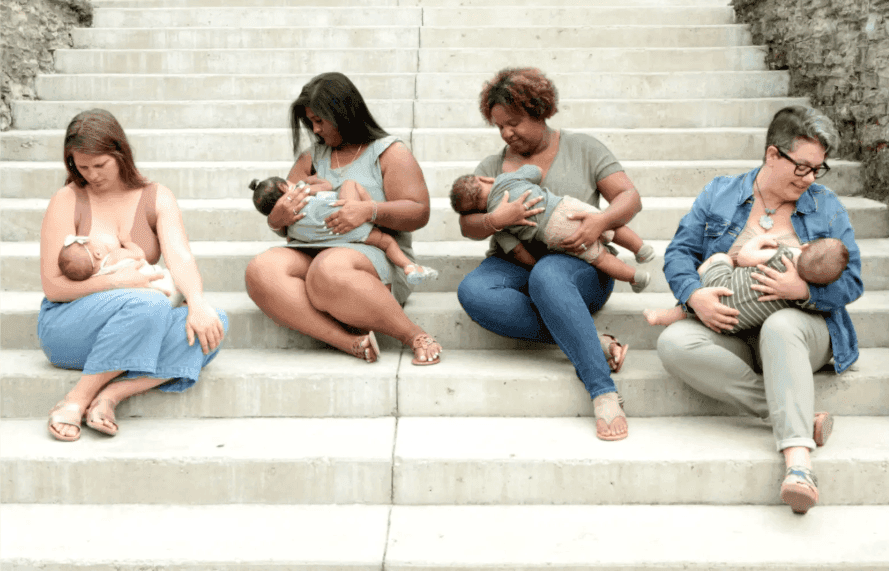 Four mothers breastfeeding their babies while sitting together on white stone steps