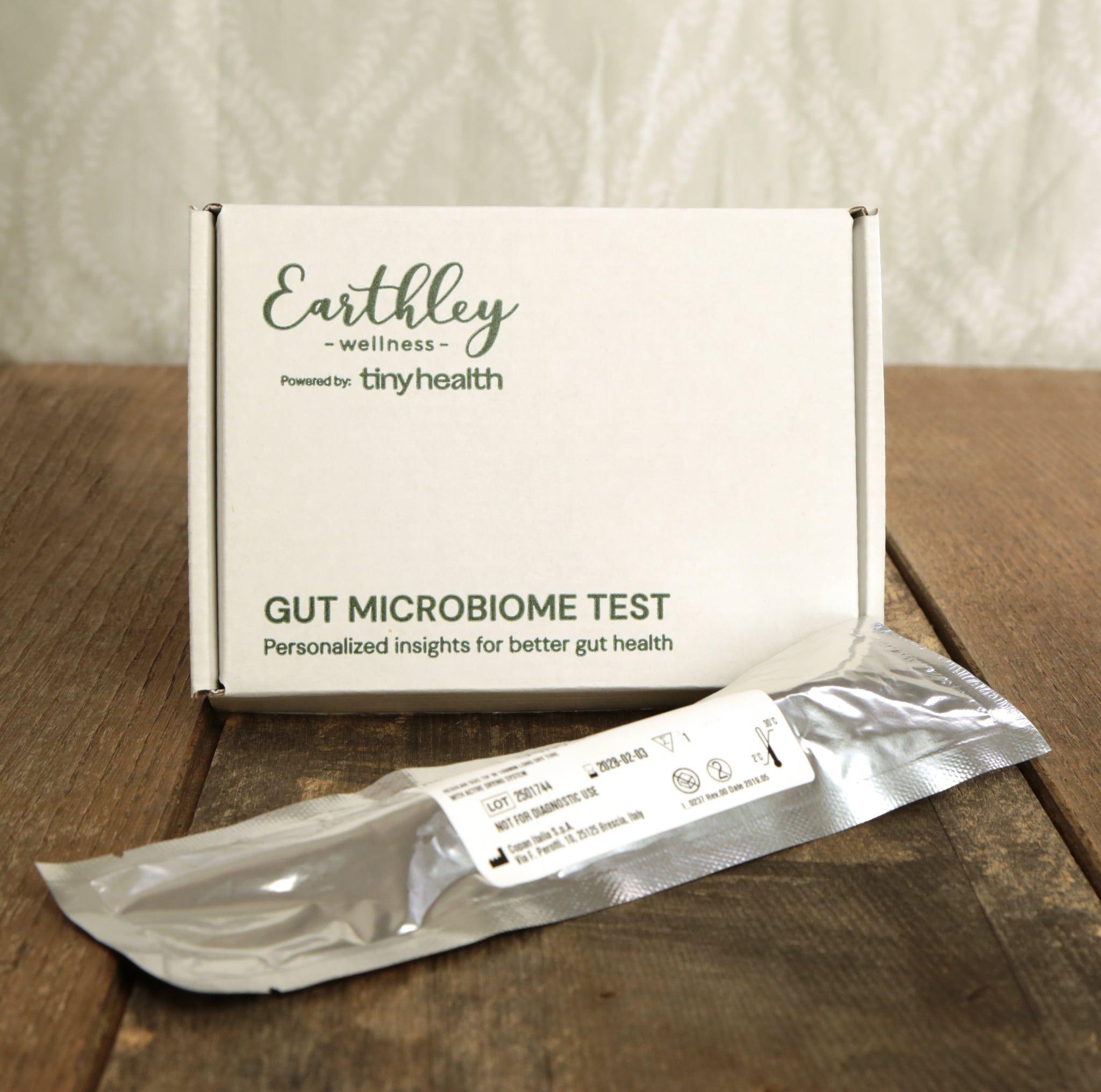 Earthley Gut Microbiome Test kit box powered by Tiny Health with sealed sample collection swab on wooden surface, offering personalized insights for better gut health