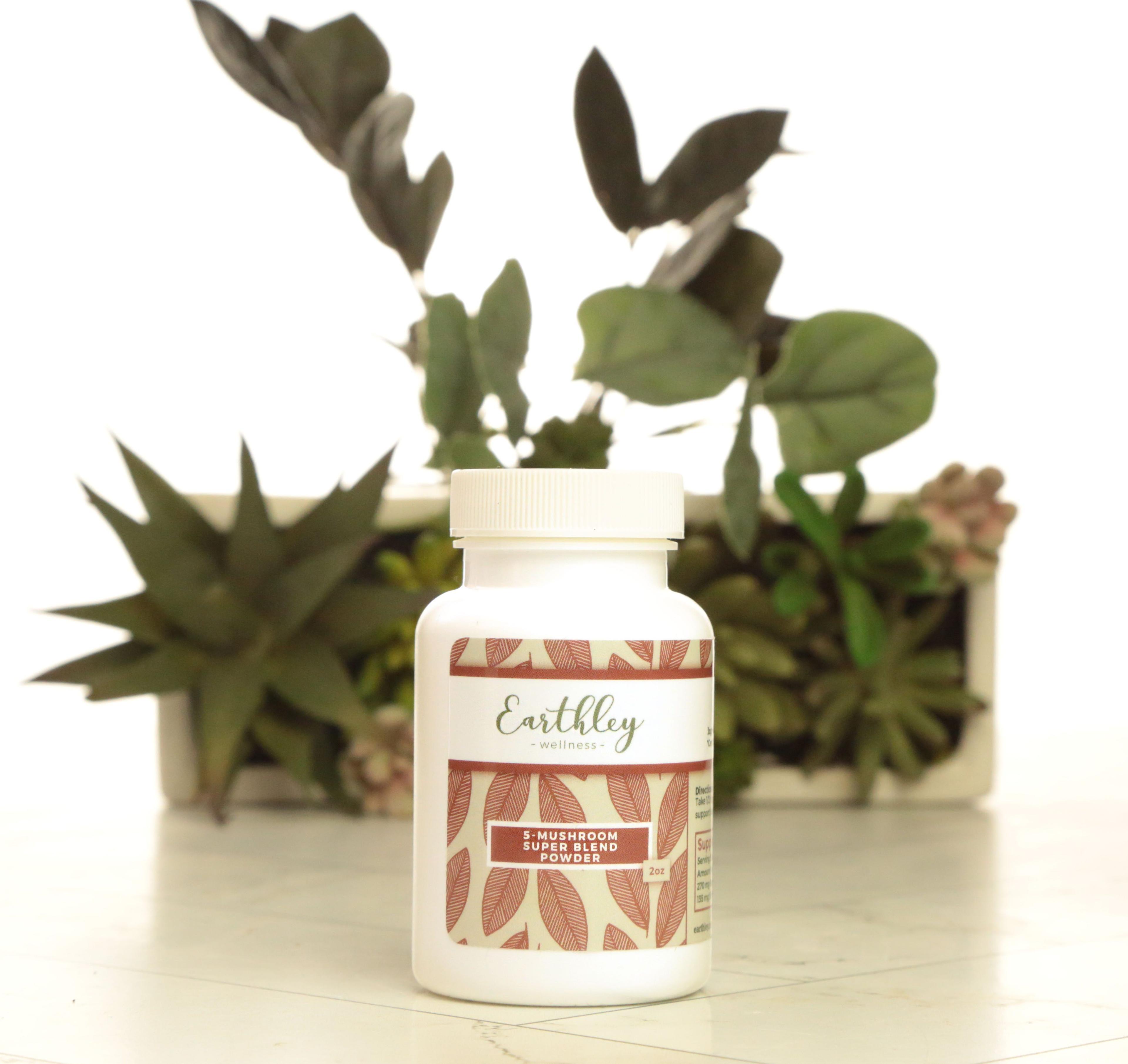 Earthley 5-Mushroom Super Blend Powder 2oz white plastic bottle with white lid and burgundy red leaf pattern label on white marble with green succulents and eucalyptus in cream planter