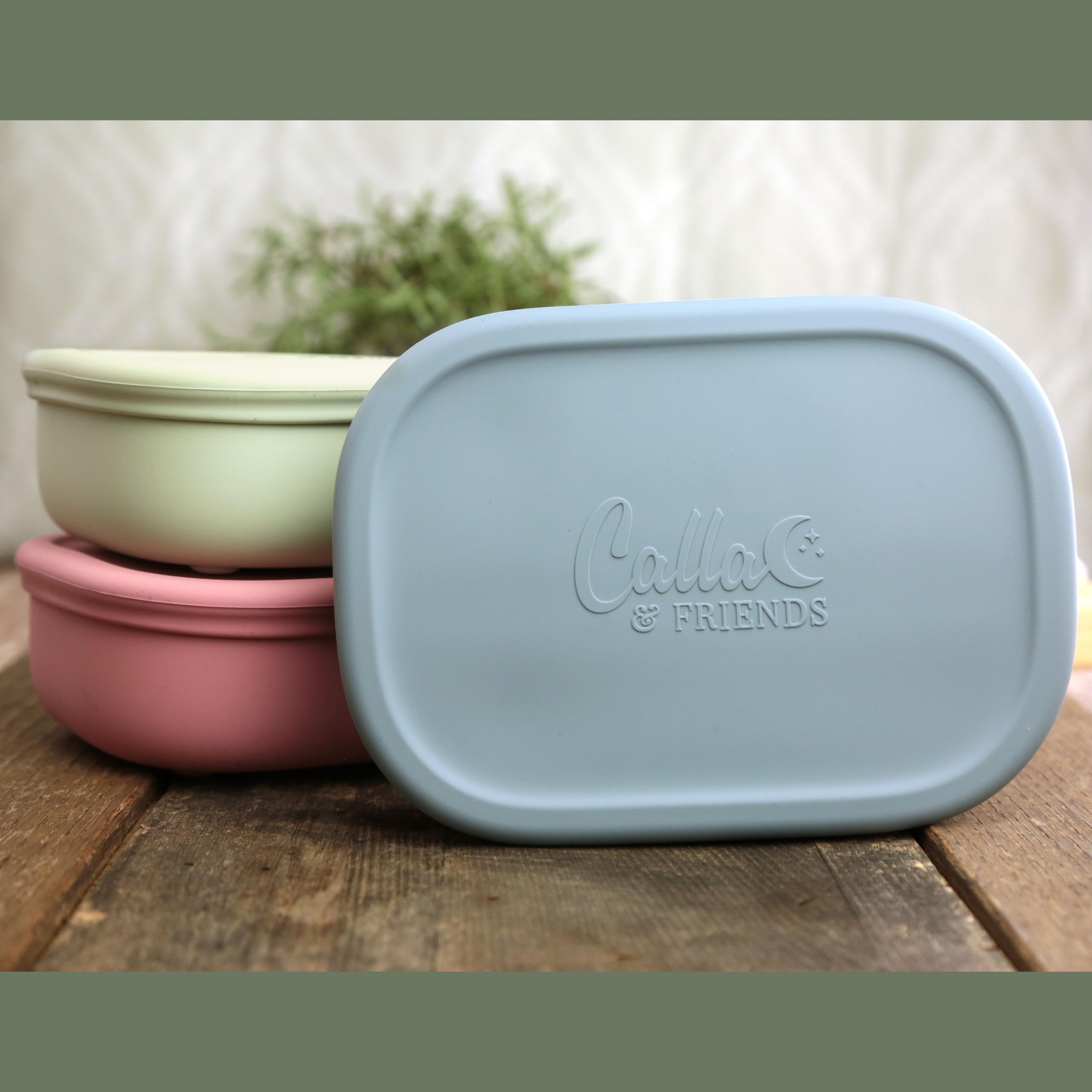 Calla and Friends silicone bento box collection showing three stacked boxes in dusty rose pink and sage green colors with blue box standing upright displaying embossed logo
