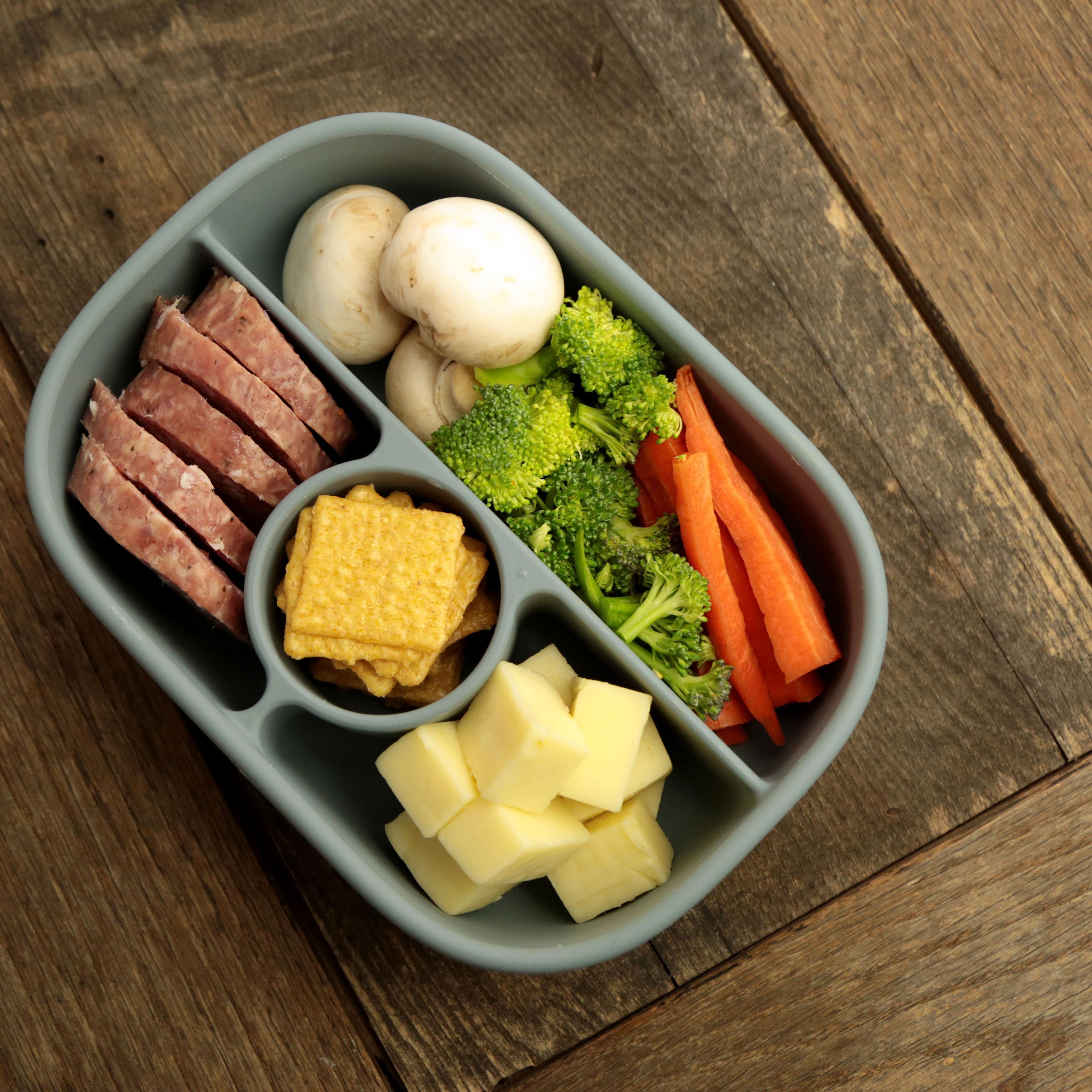 Calla and Friends silicone bento box in sage green color opened showing compartments filled with fresh salad, mushrooms, vegetables, hard boiled egg, yogurt dip, strawberries and blueberries