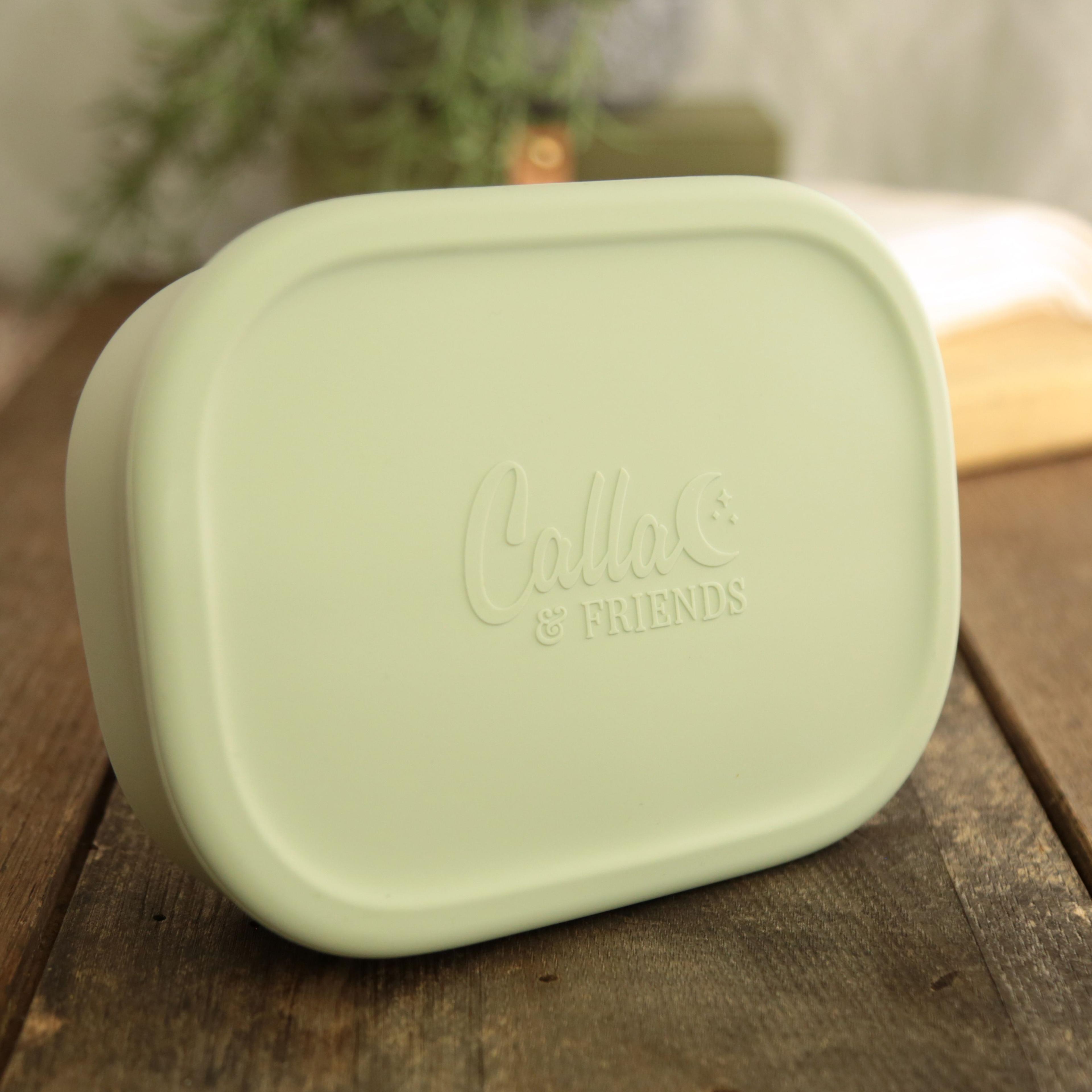 Calla and Friends silicone bento box in sage green color showing closed lid with embossed logo on wooden surface