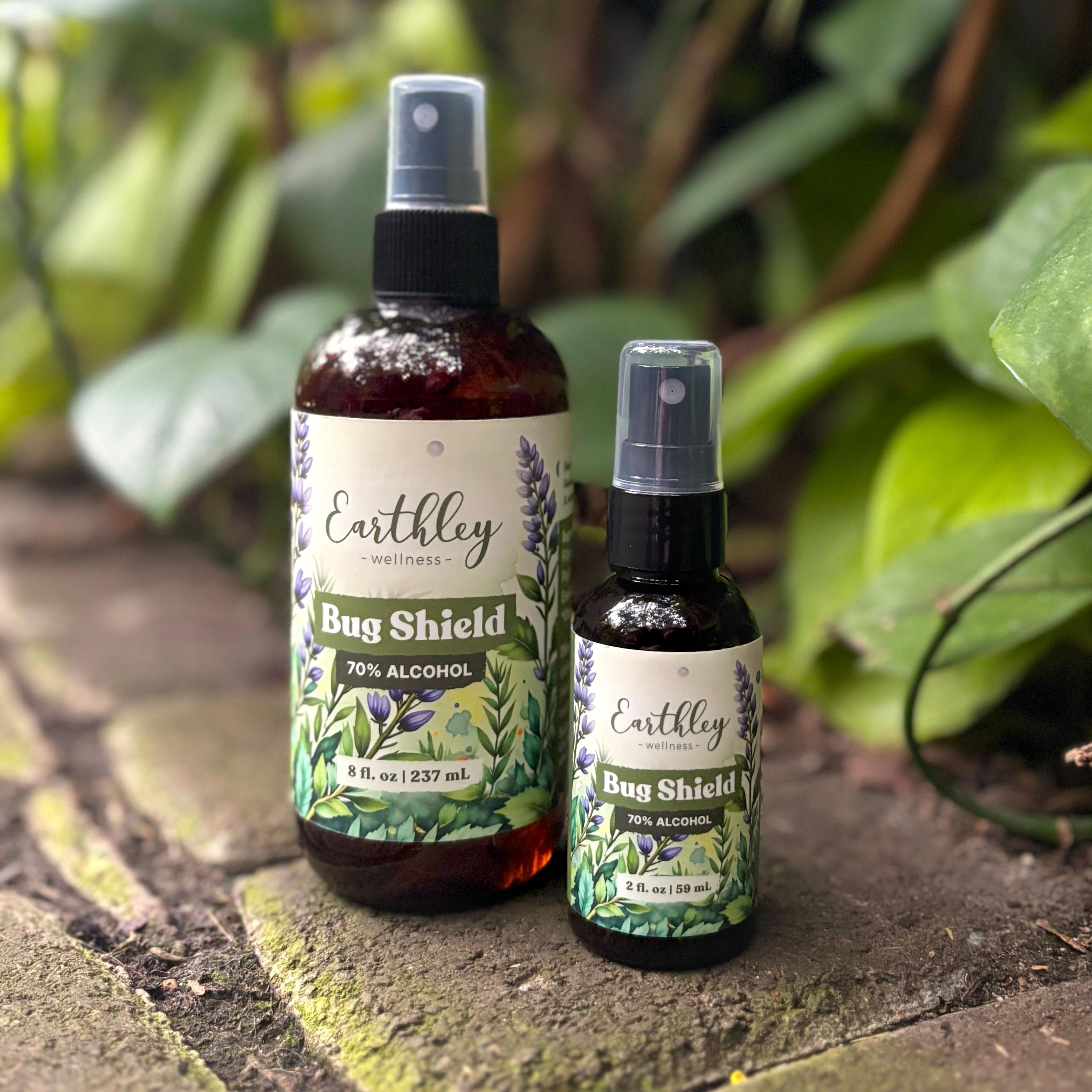 Two Earthley Bug Shield spray bottles in 8oz and 2oz sizes with botanical labels, displayed outdoors on wooden surface