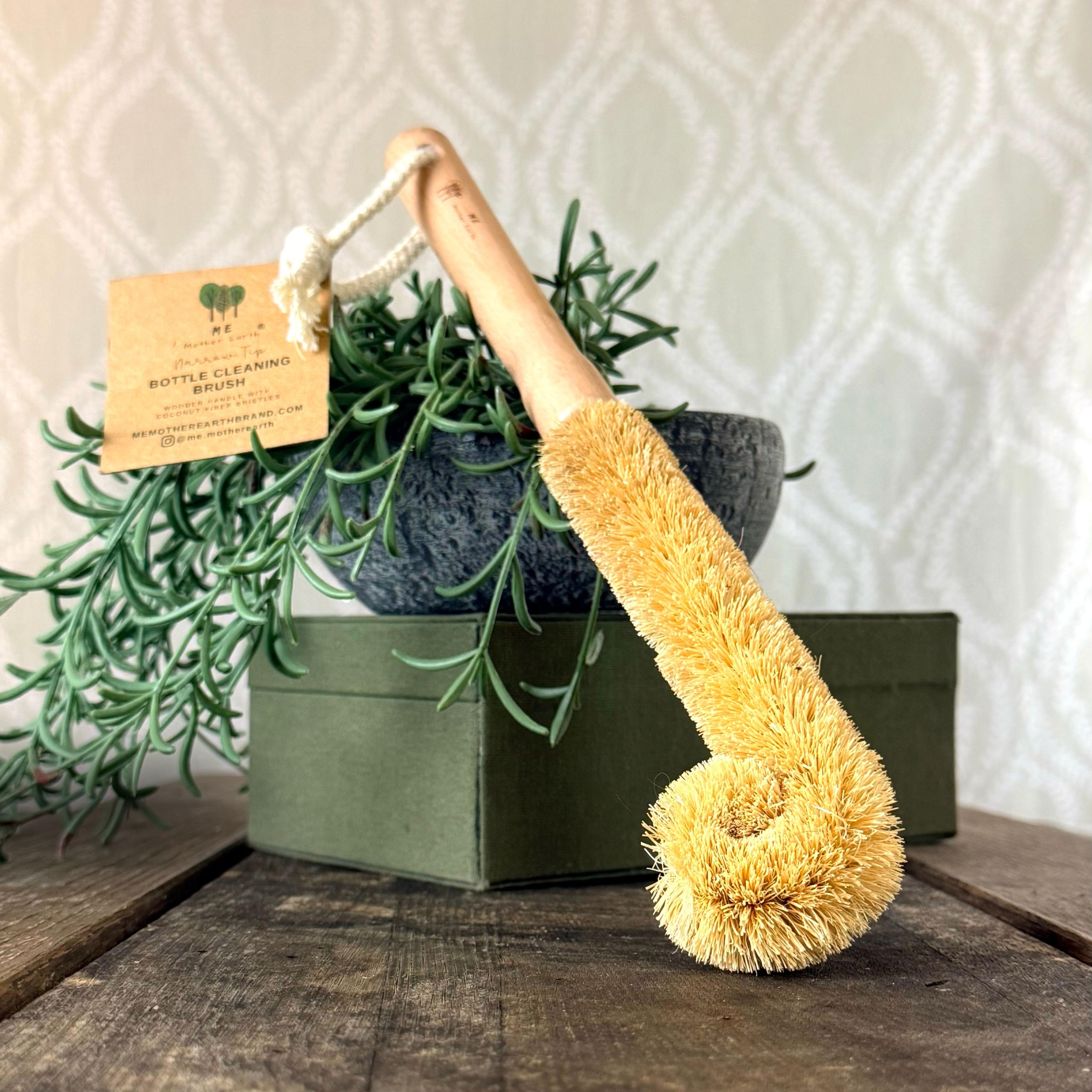 Coconut Bottle Cleaning Brush leaned against a plant setting