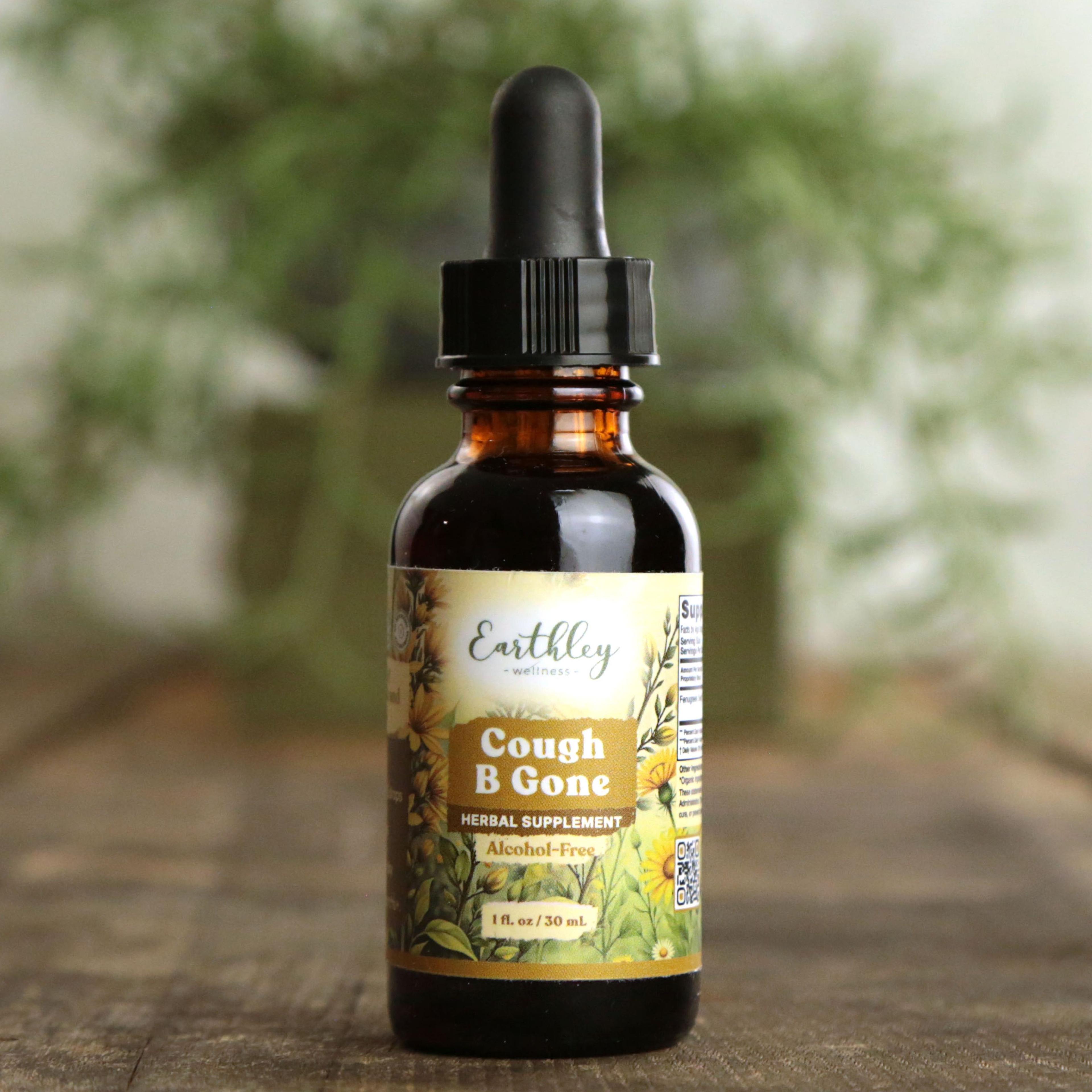 Earthley Cough B Gone Alcohol-Free 1 fl oz amber dropper bottle with yellow daisy and botanical label on rustic wood surface with blurred green plant in background