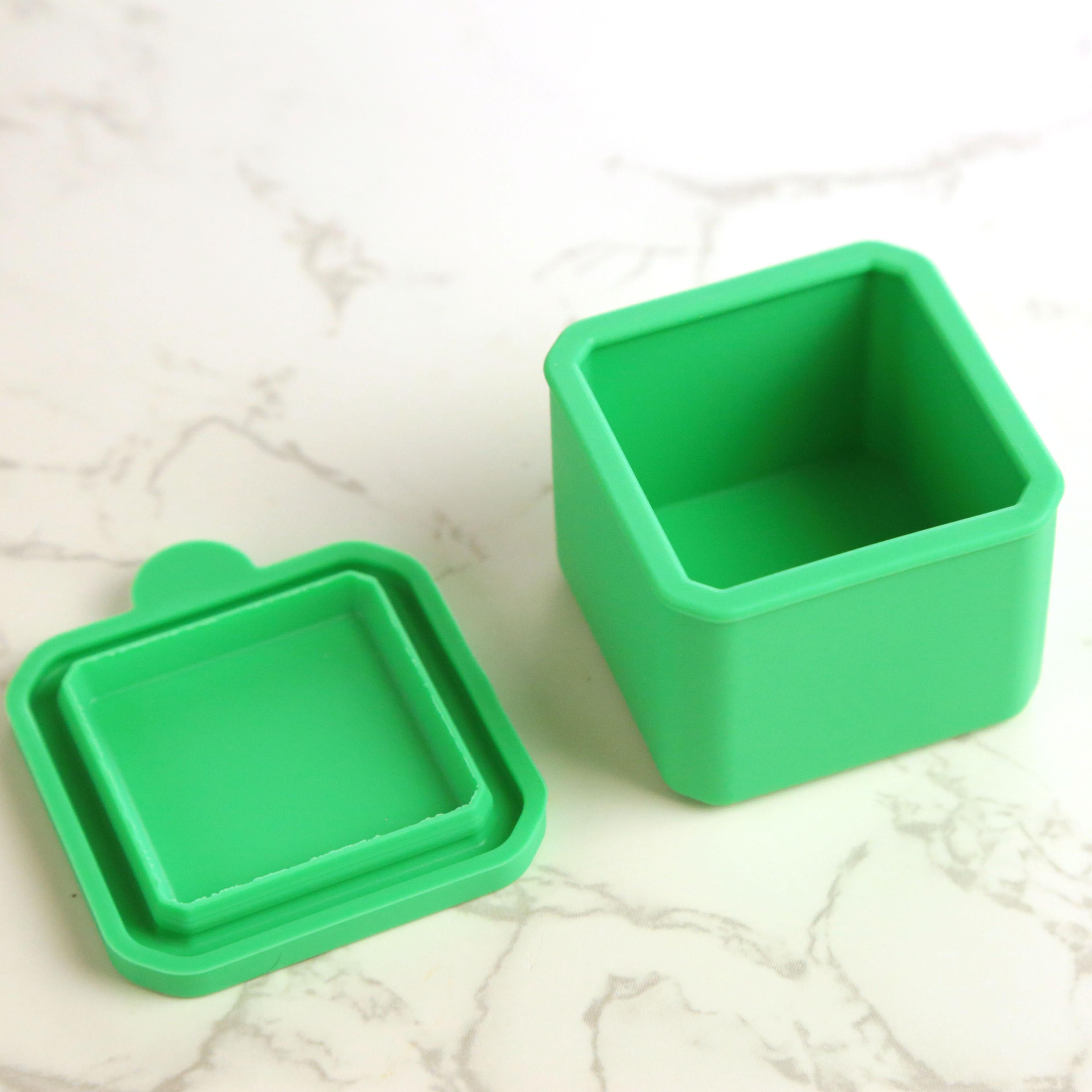 Green silicone square container with lid removed, shown open on marble surface