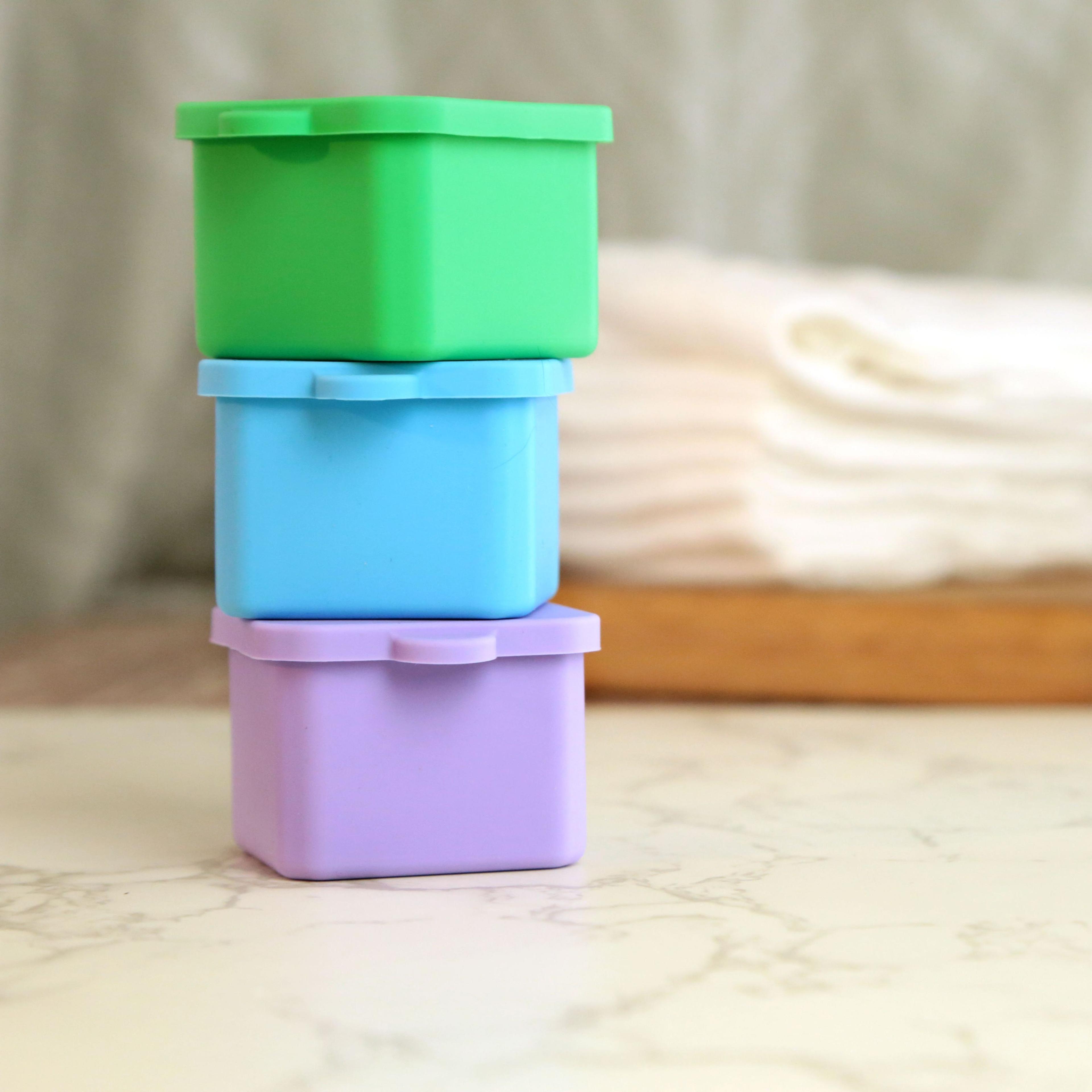 Three stacked silicone containers in green, blue, and lavender on marble surface