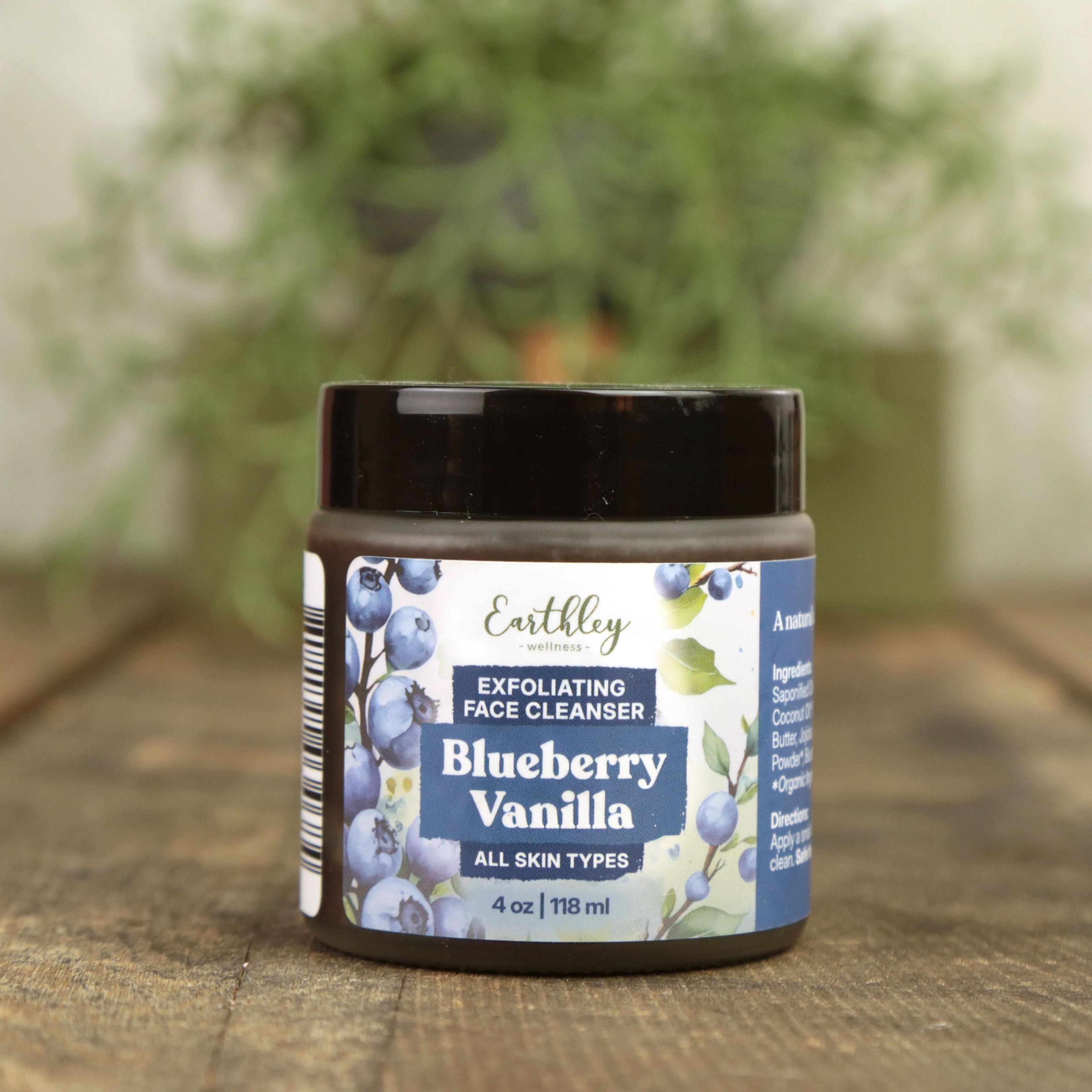 Earthley Blueberry Vanilla Exfoliating Face Cleanser jar with black lid on wooden surface, green plants in background