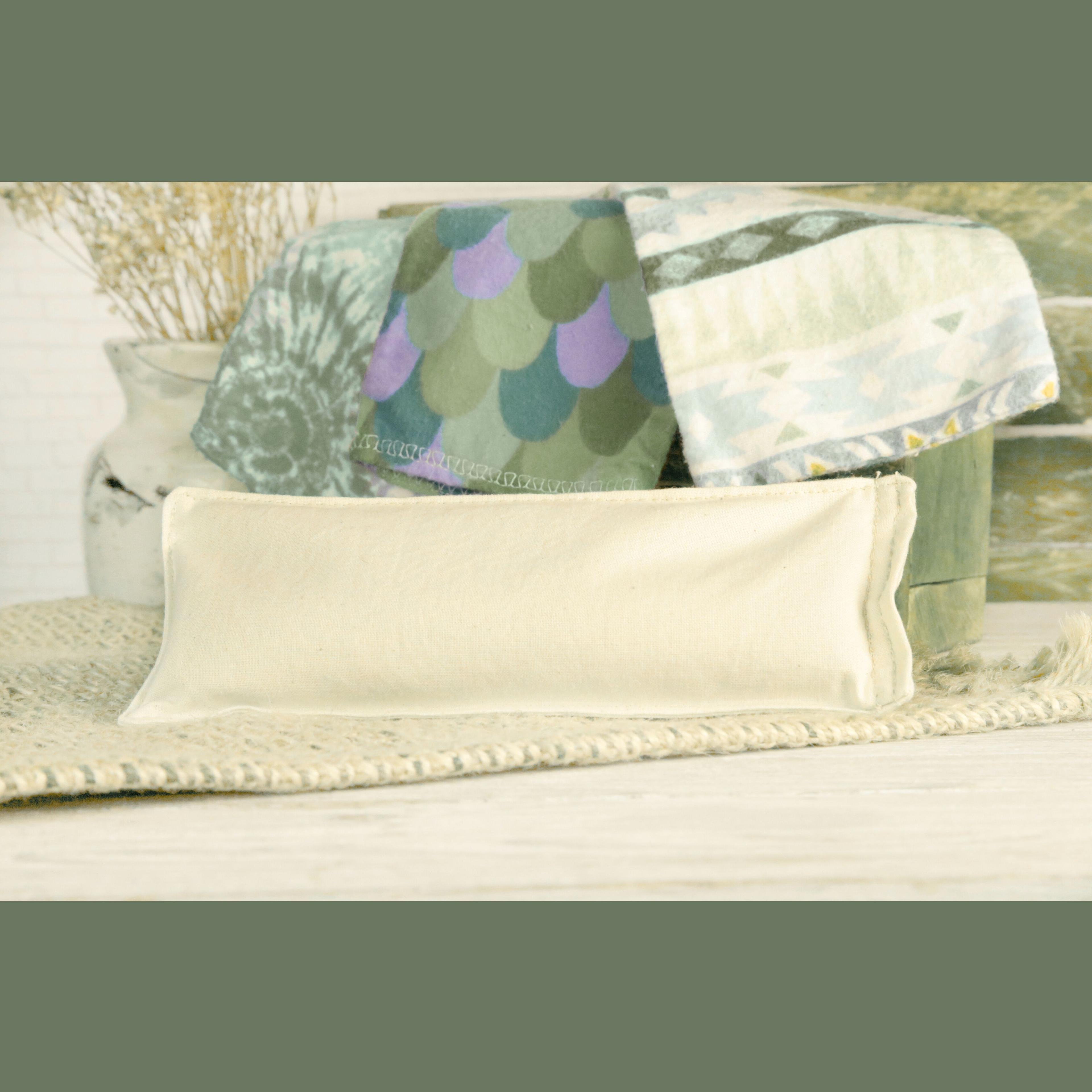Earthley Flax Heating Pad in natural cream unbleached cotton fabric on tan woven placemat with teal purple and sage patterned blankets and cream ceramic vase with dried wheat