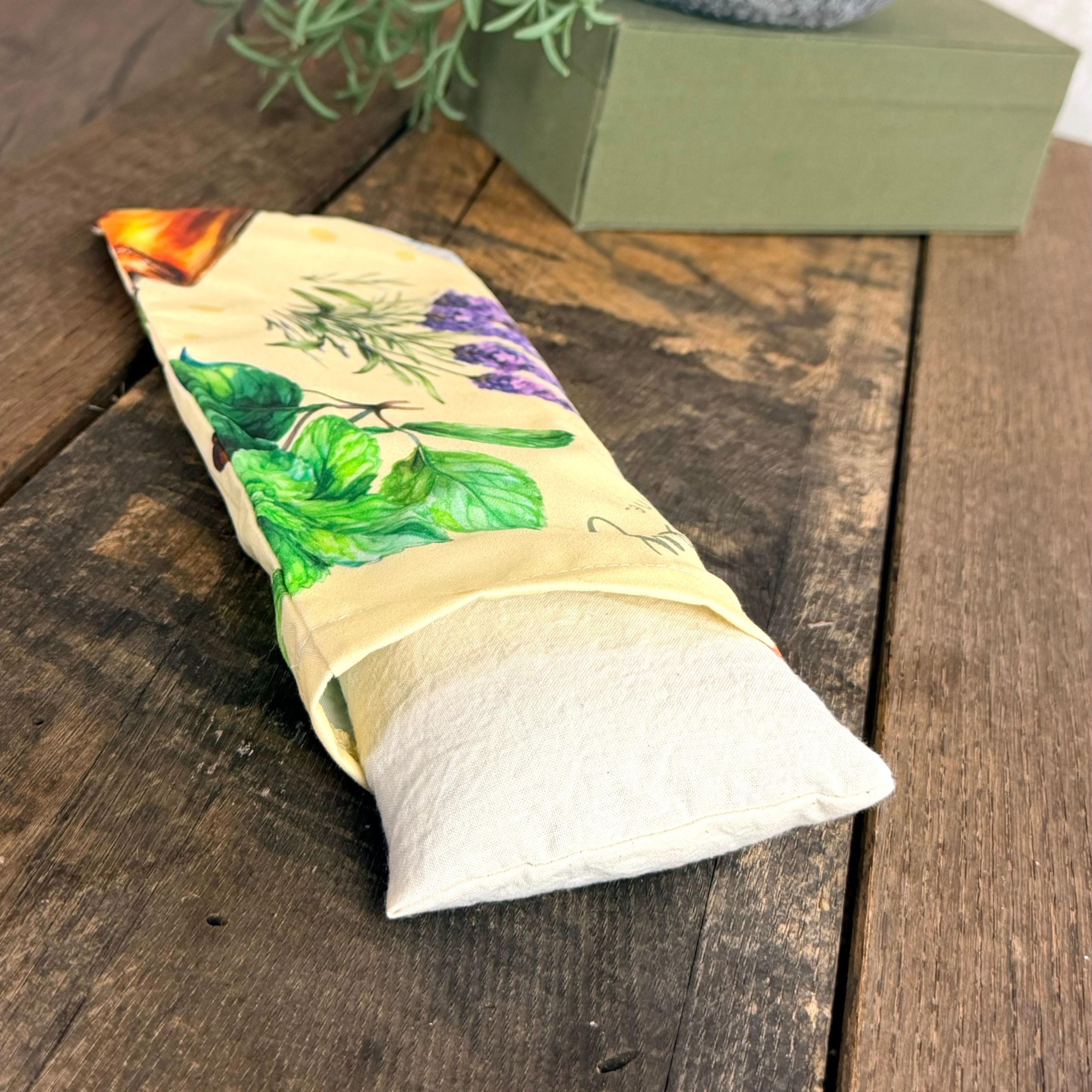 Herbal eye pillow with botanical print featuring lavender, mint leaves, and orange flowers on rustic wooden surface