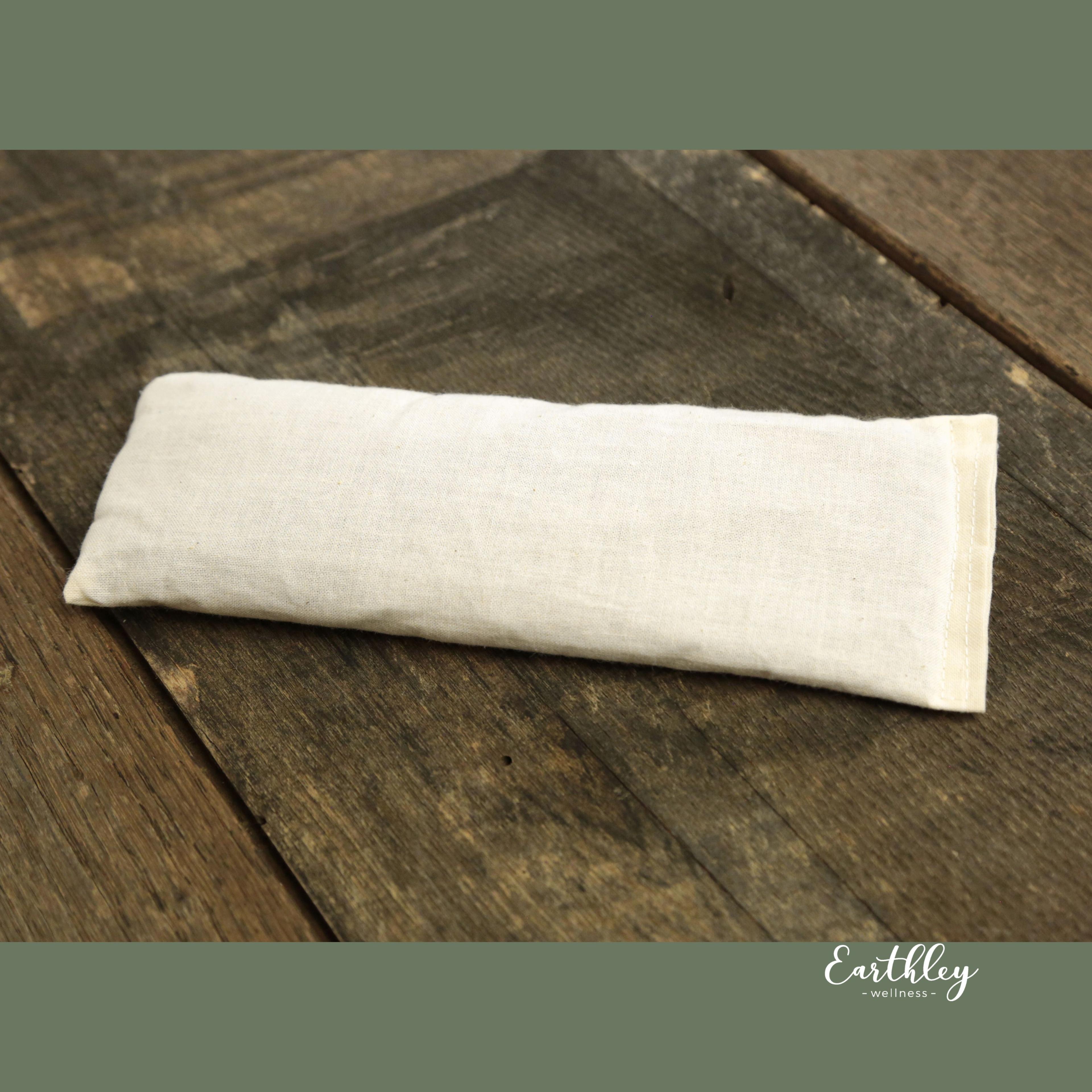 Natural linen eye pillow resting on weathered wooden surface with Earthley Wellness branding