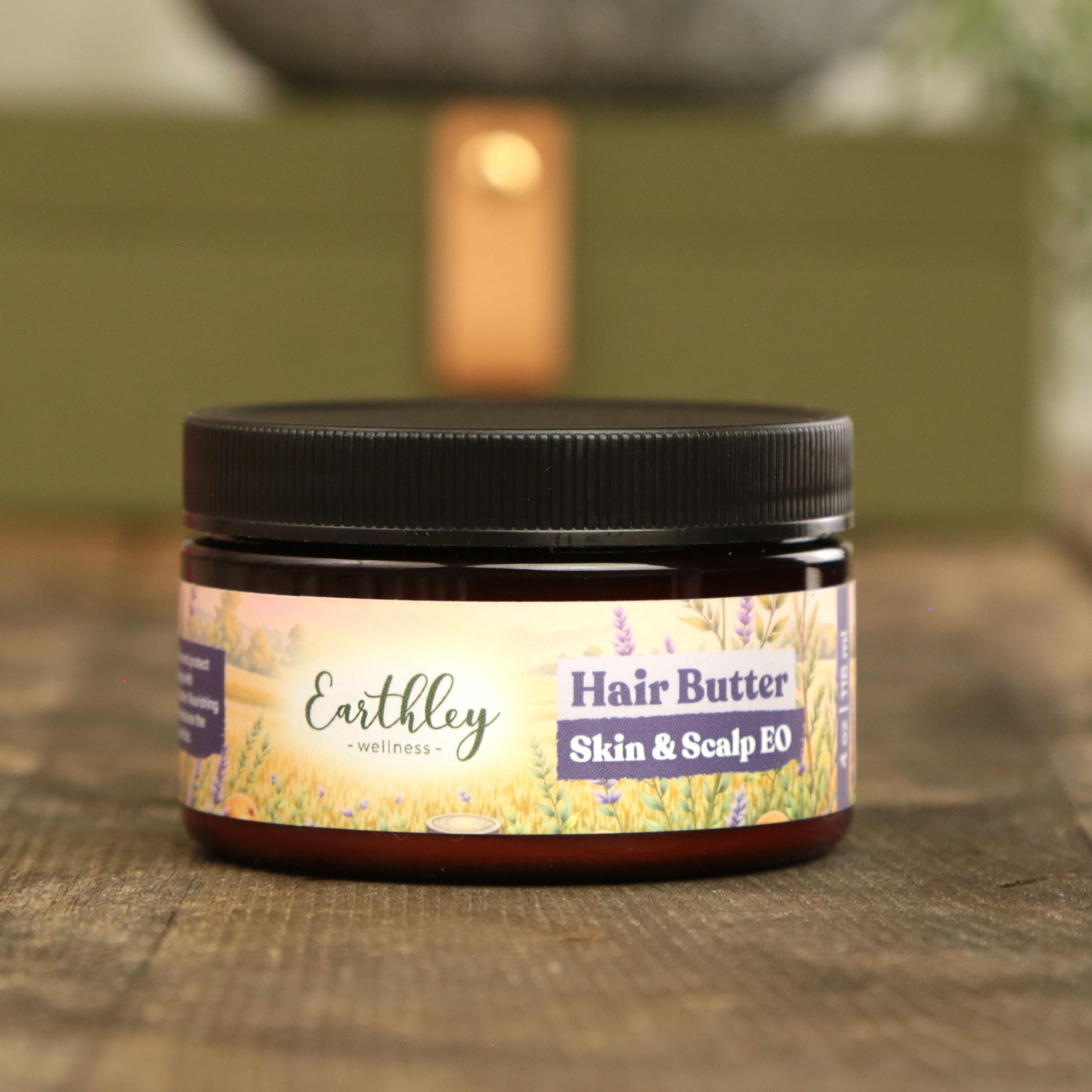 Earthley Hair Butter Skin and Scalp EO 4 oz in amber jar with black lid featuring lavender field sunset label on wooden surface with warm candlelight glow in background