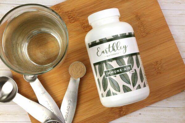 Immune-Aid supplement bottle with measuring spoons and glass of water on wooden board