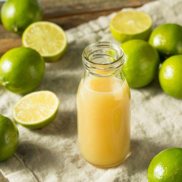 Fresh lime juice in a glass bottle surrounded by whole and halved limes on linen cloth