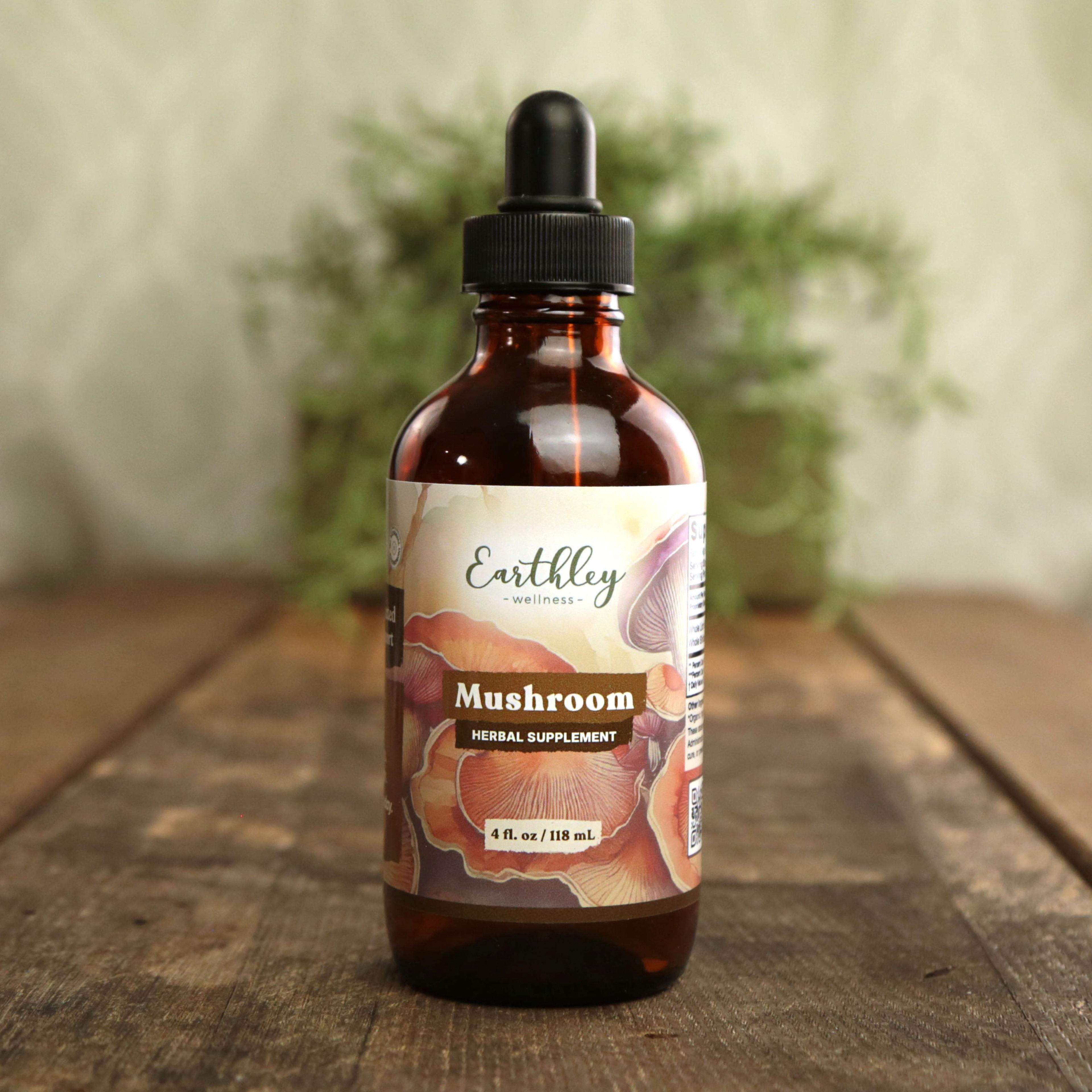 Earthley Mushroom 4 fl oz amber dropper bottle with botanical label featuring illustrated pink and coral mushrooms, labeled as Herbal Supplement, on wooden surface with greenery in background
