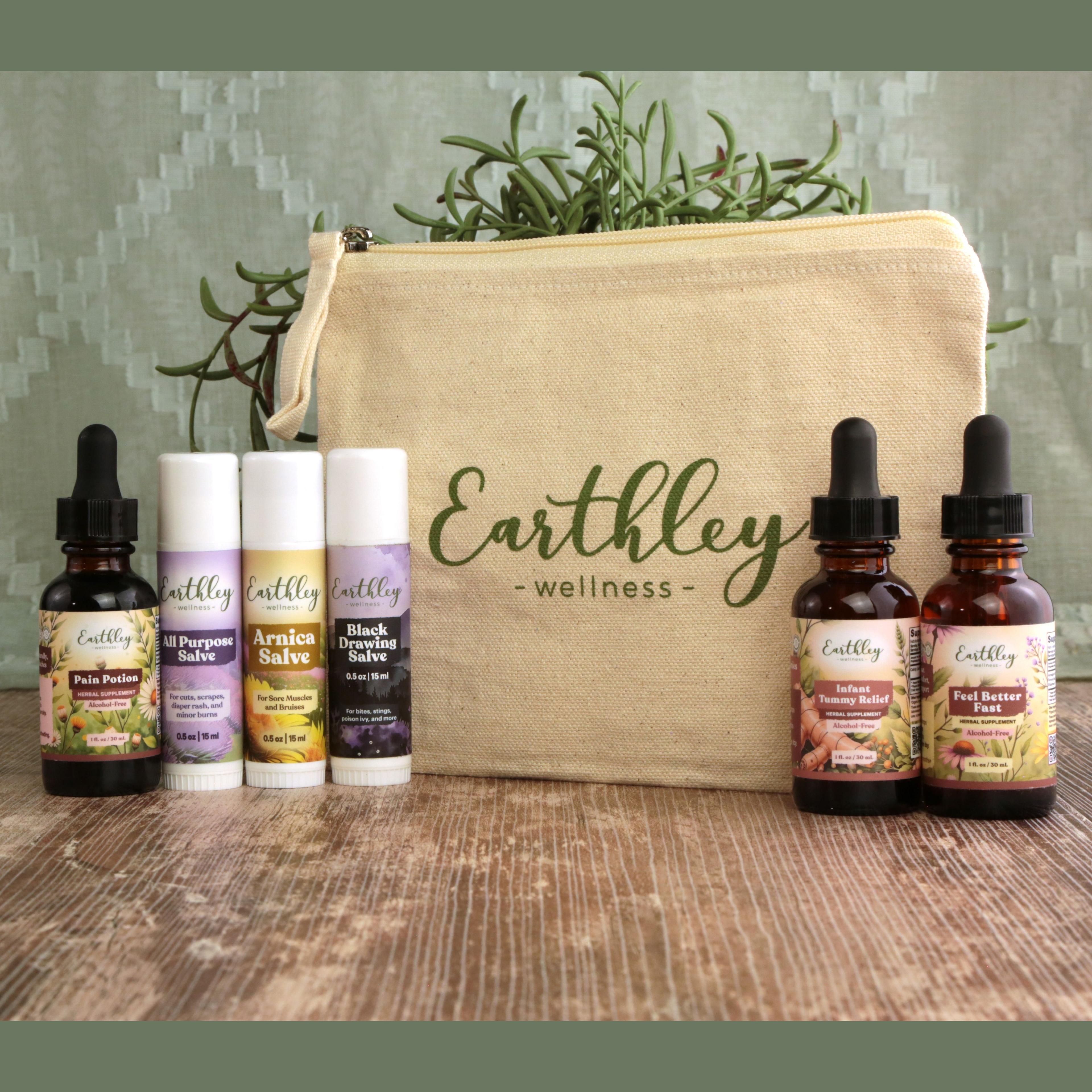 Earthley Natural First Aid Bundle with cream canvas zipper pouch amber dropper bottles white salve tubes and green rosemary on rustic wooden surface partially visible