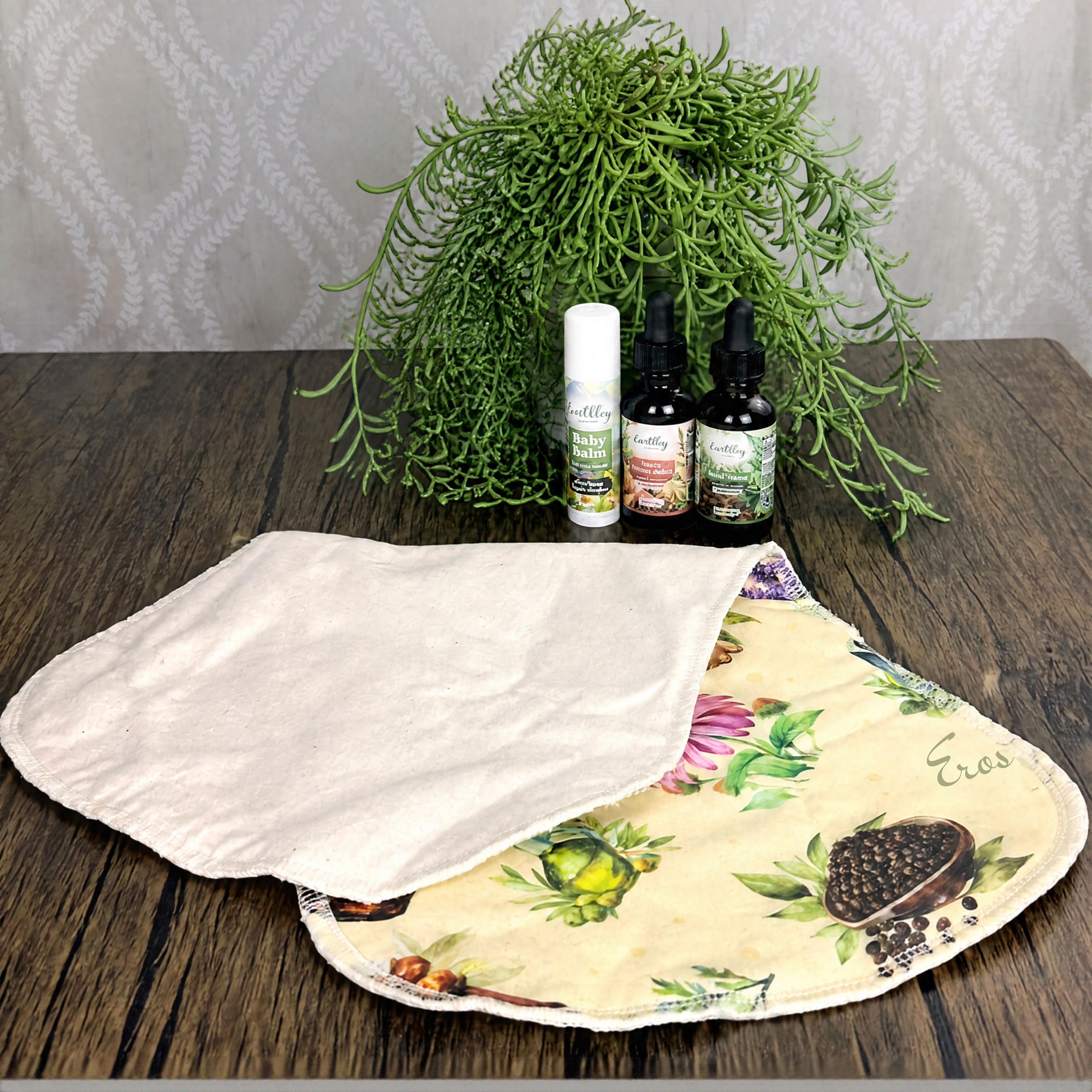 Earthley Baby Balm stick and two herbal tinctures with floral burp cloth on wood table
