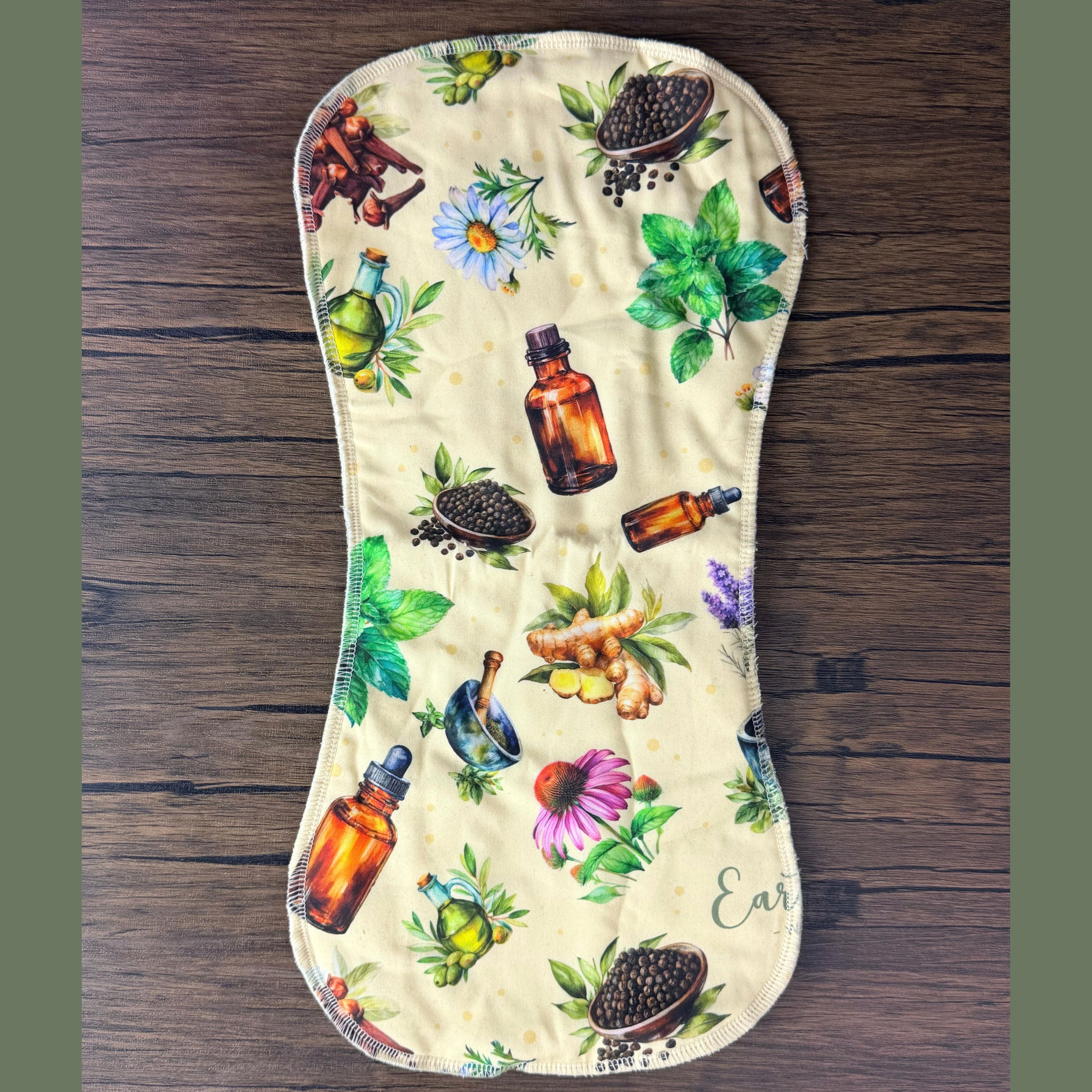 Earthley burp cloth with herbal print featuring tincture bottles, herbs, and botanicals on cream fabric