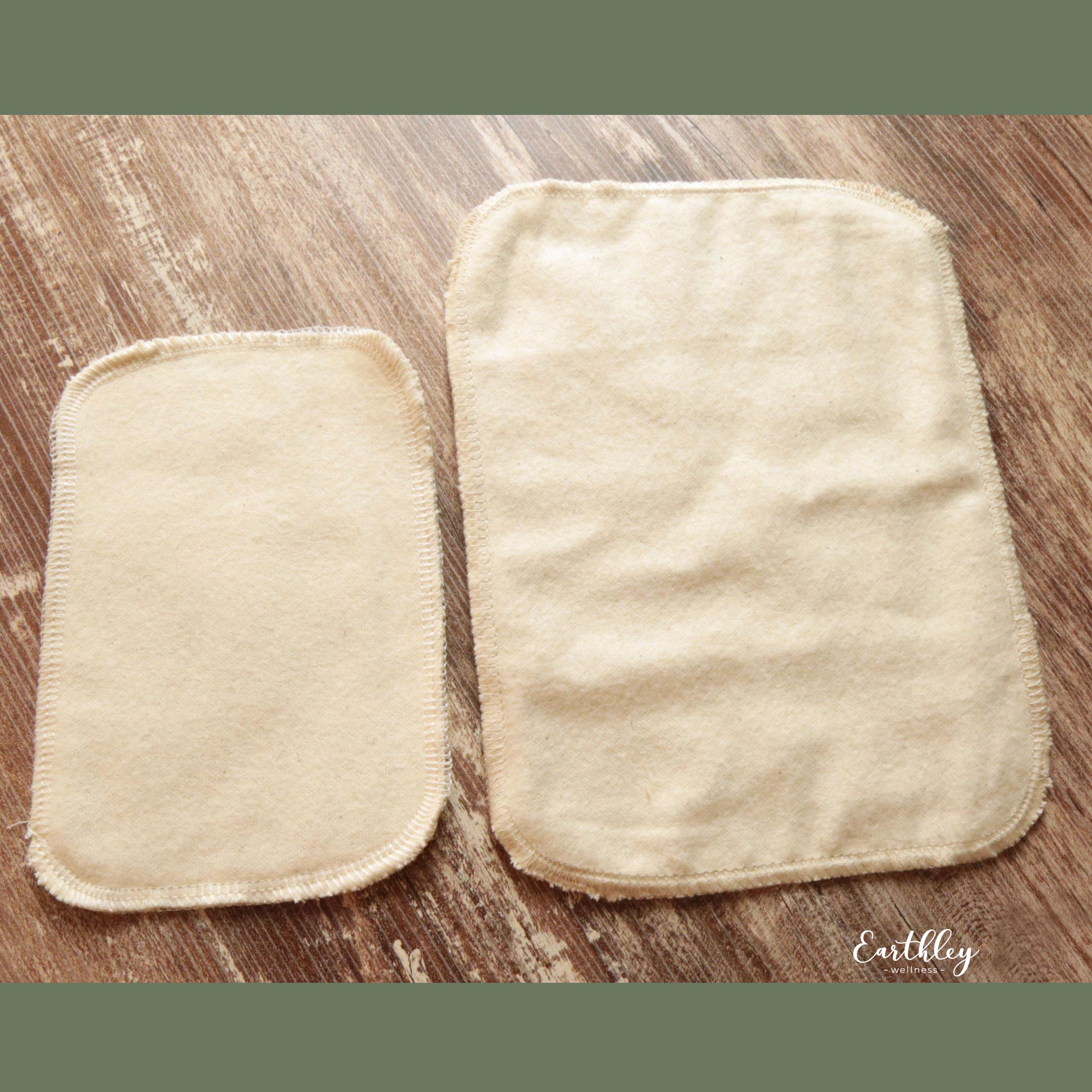 Two natural unbleached cotton reusable cloth wipes in small and large sizes on wood surface