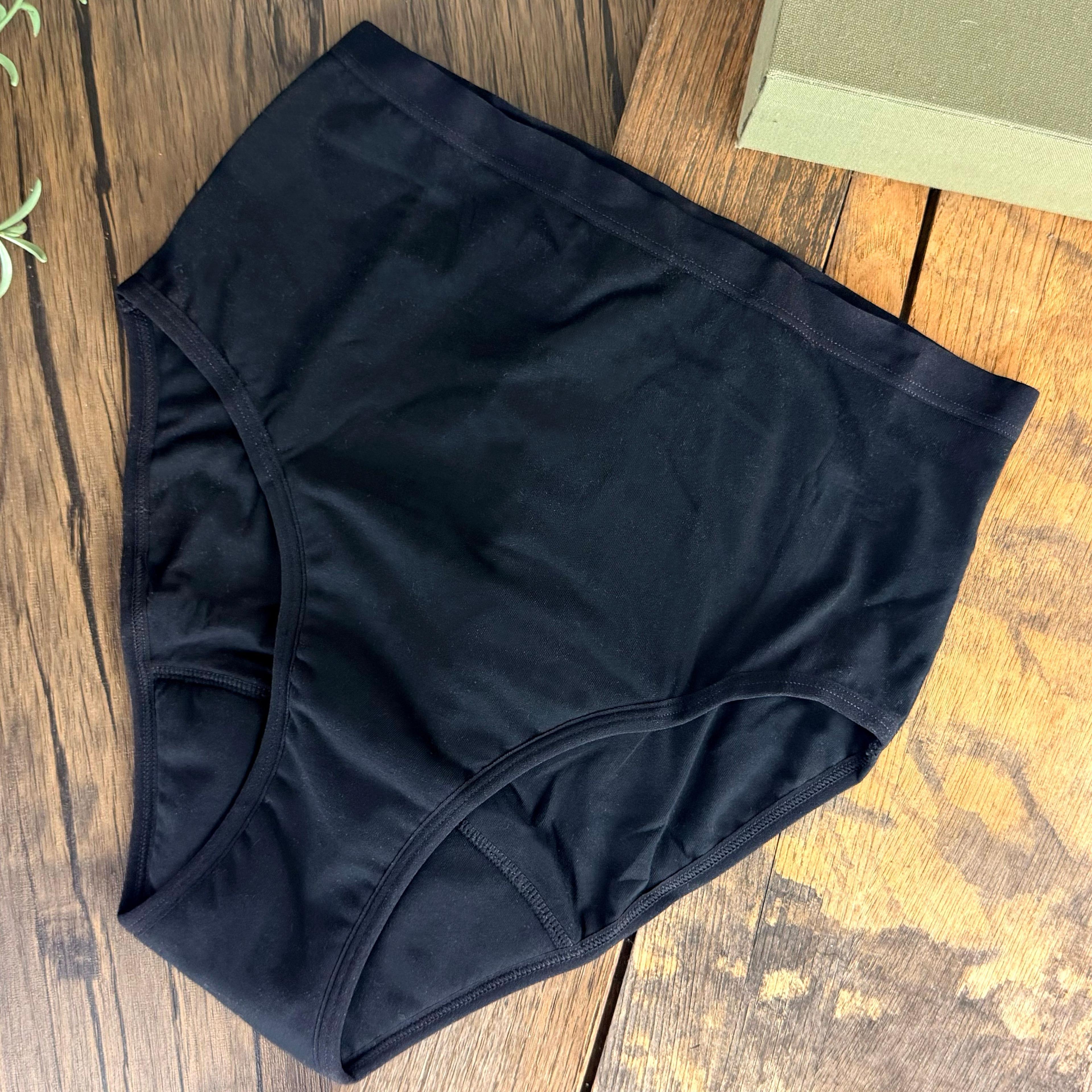 Black high-waist period underwear laid flat on rustic wood surface