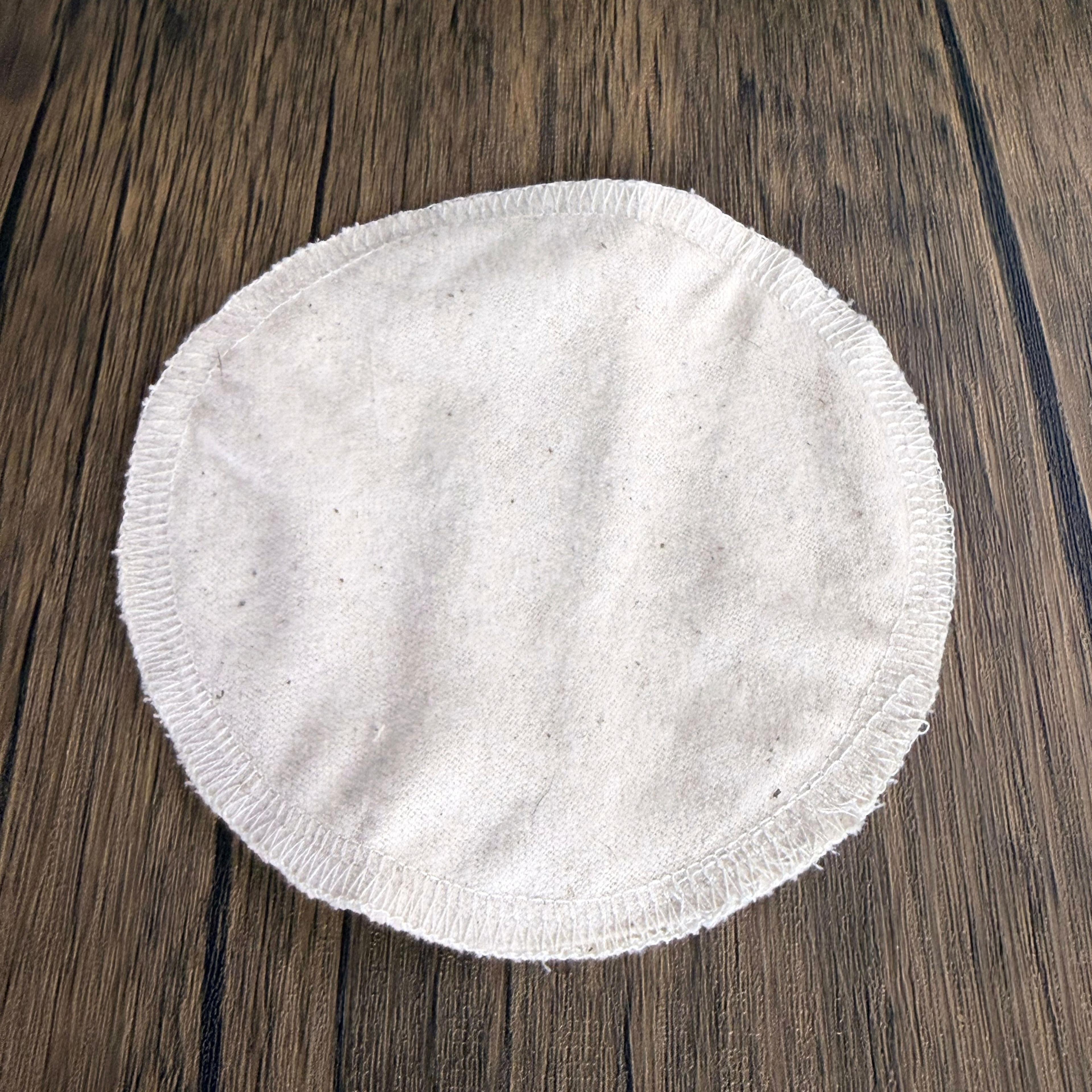 Round white reusable cotton nursing pad with serged edges on wood surface