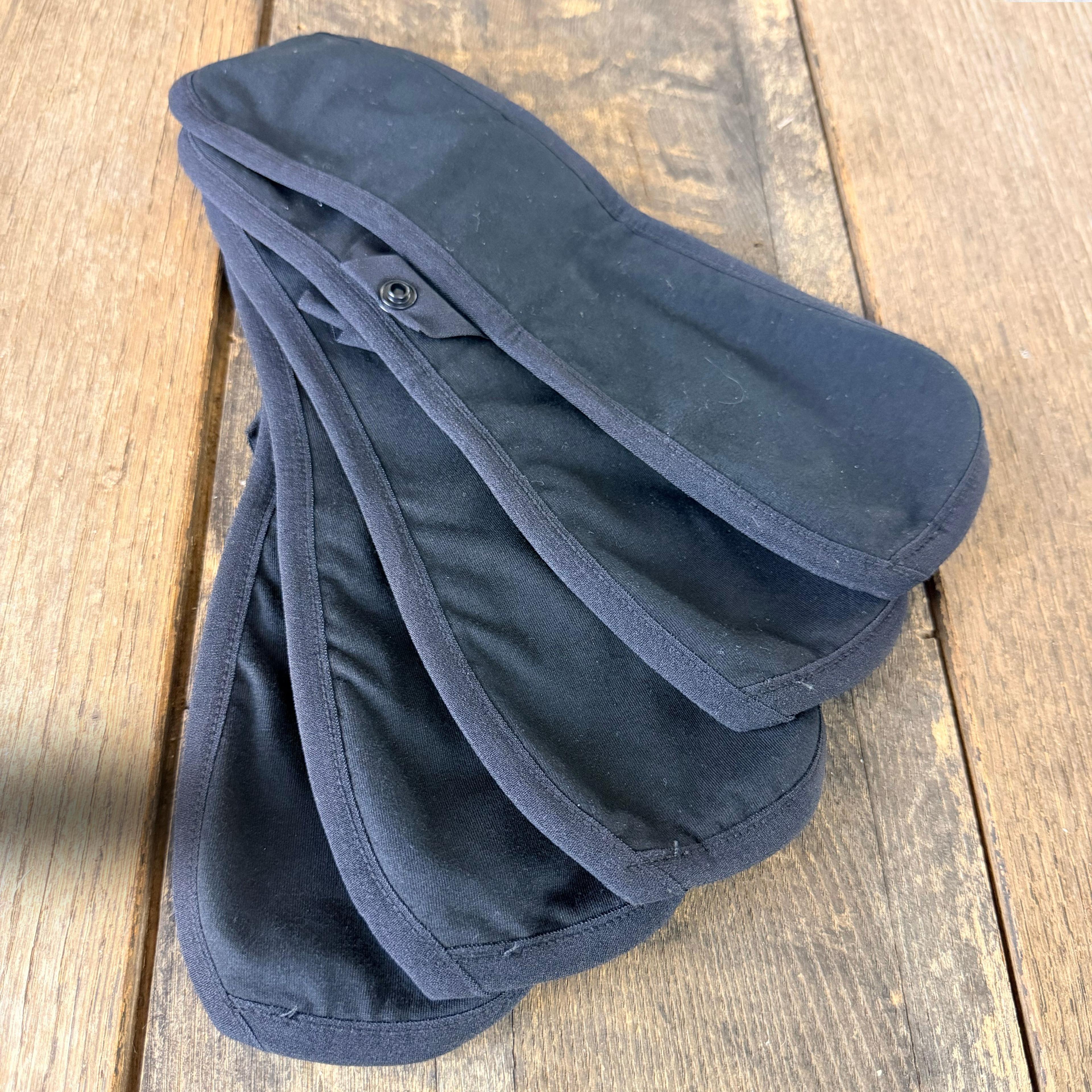 Five black reusable cloth menstrual pads with snap closure on wooden surface