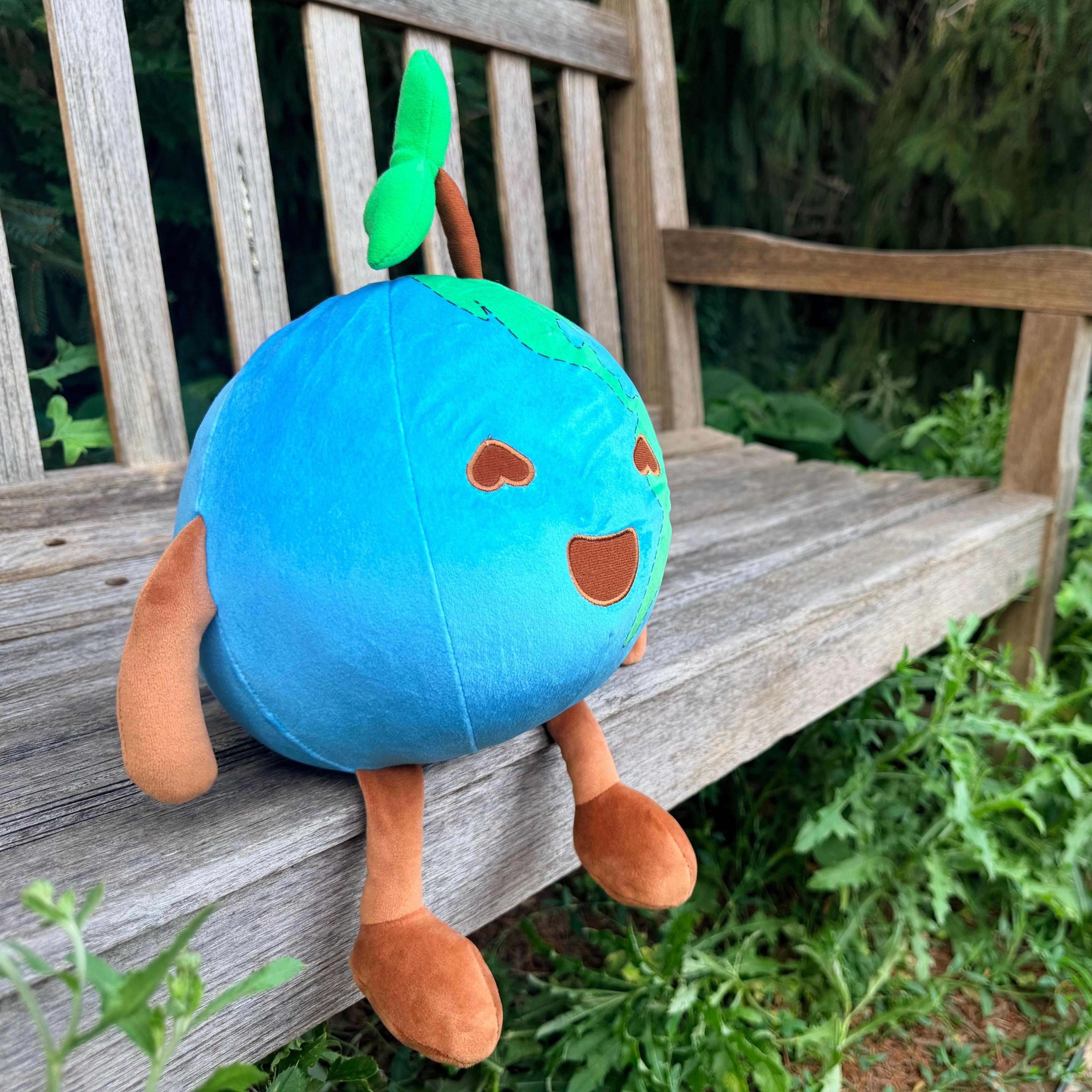 Earthley mascot plush toy with blue globe body, green sprout, and smiling face on wooden bench