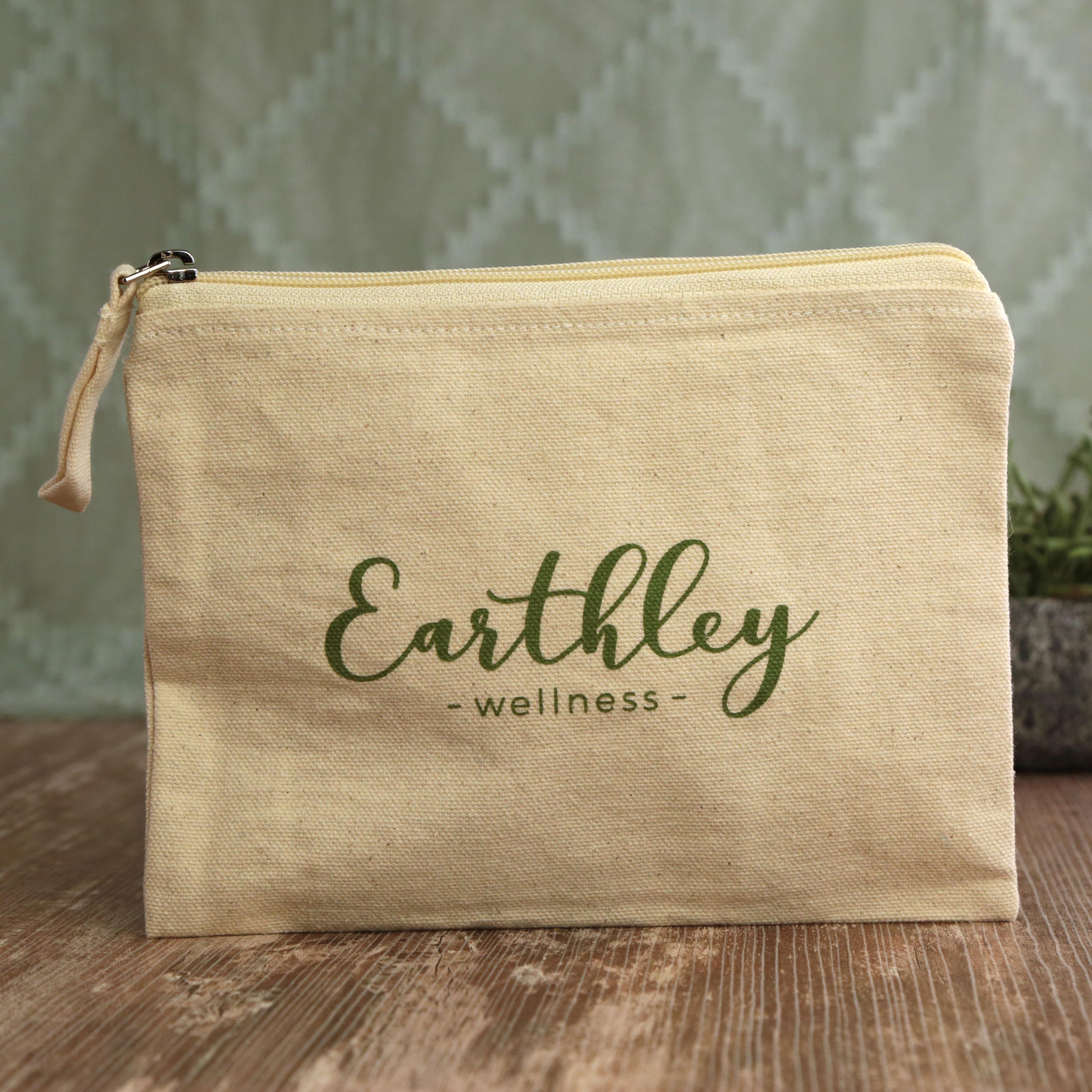 Earthley Tincture Carrying Bag back view showing natural cream canvas zippered pouch with dark green Earthley Wellness logo on rustic wooden surface with sage chevron background