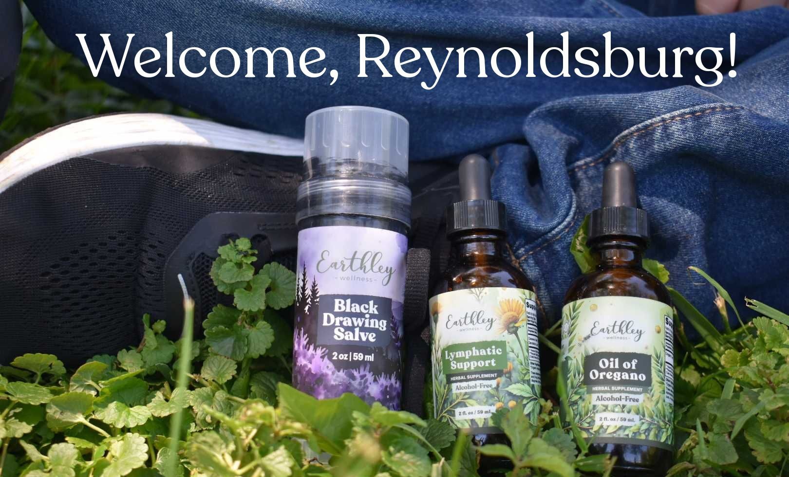 Earthley Wellness Black Drawing Salve, Lymphatic Support, and Oil of Oregano nestled in green herbs