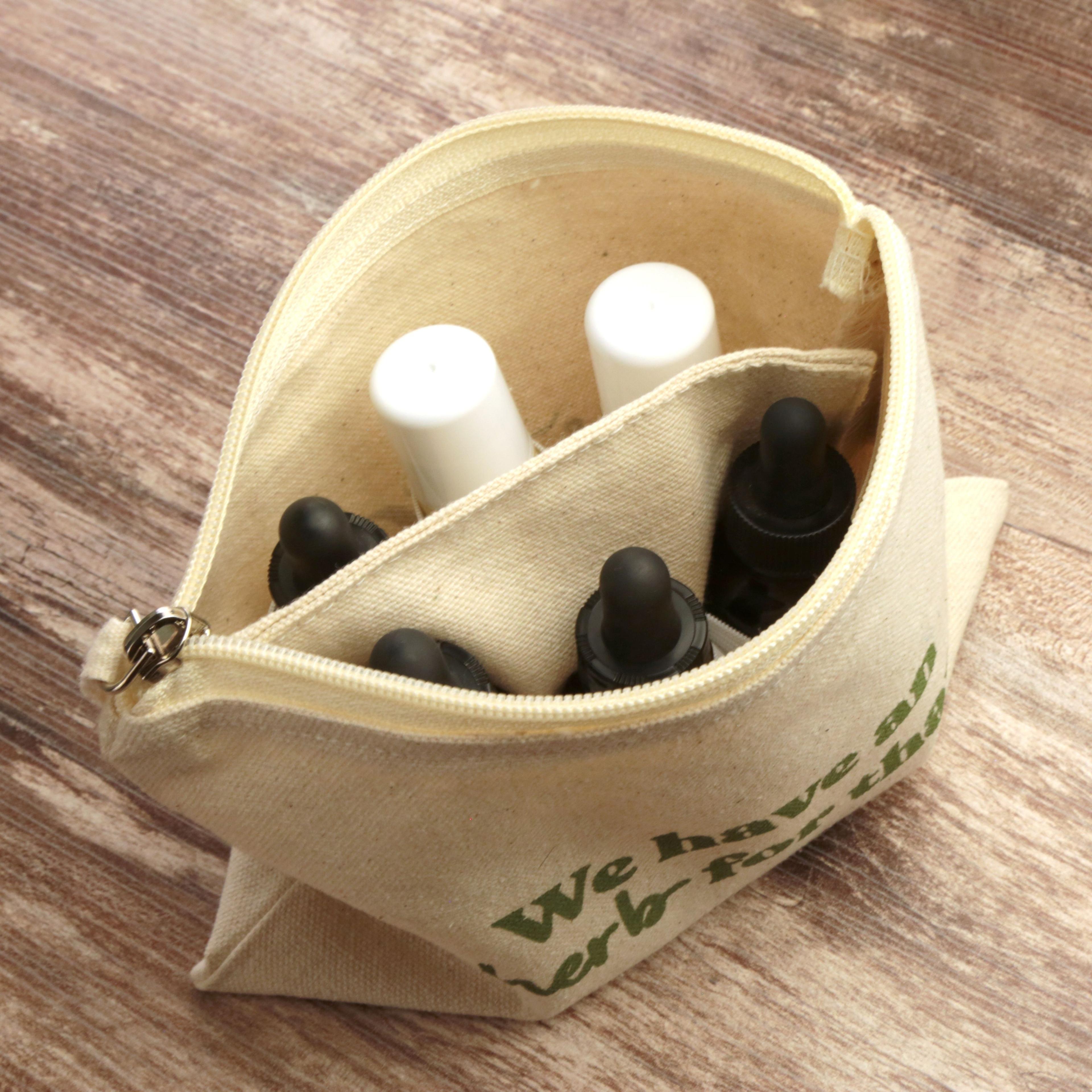 Open canvas zipper pouch with We have an herb for that text showing interior compartments containing Earthley tincture bottles and salve sticks for travel, on wooden surface