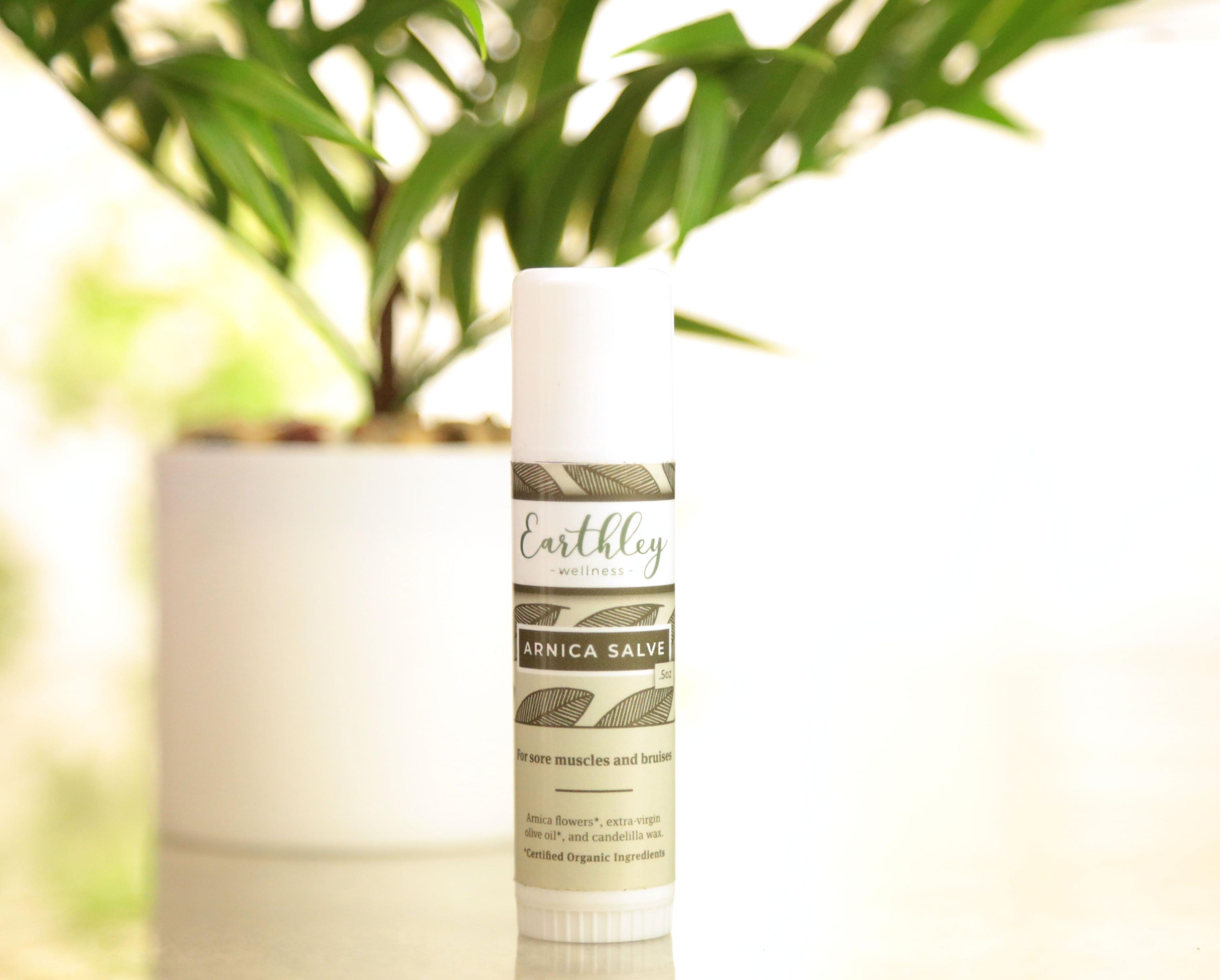 Earthley Arnica Salve twist-up tube product photo with soft natural lighting and botanical background