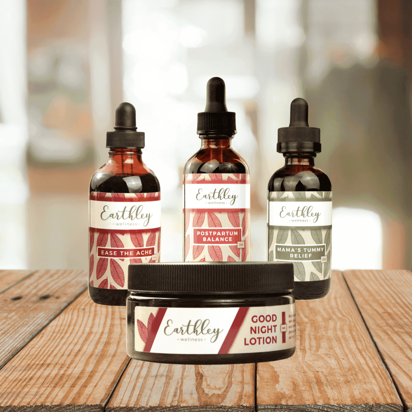 Earthley Birthworker Bundle featuring three amber glass dropper bottles with coral red leaf labels and amber Good Night Lotion jar with black lid arranged on wooden surface