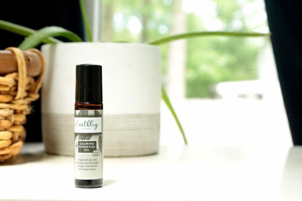 Calming Essential Oil roller bottle with gray leaf label on white surface with plants
