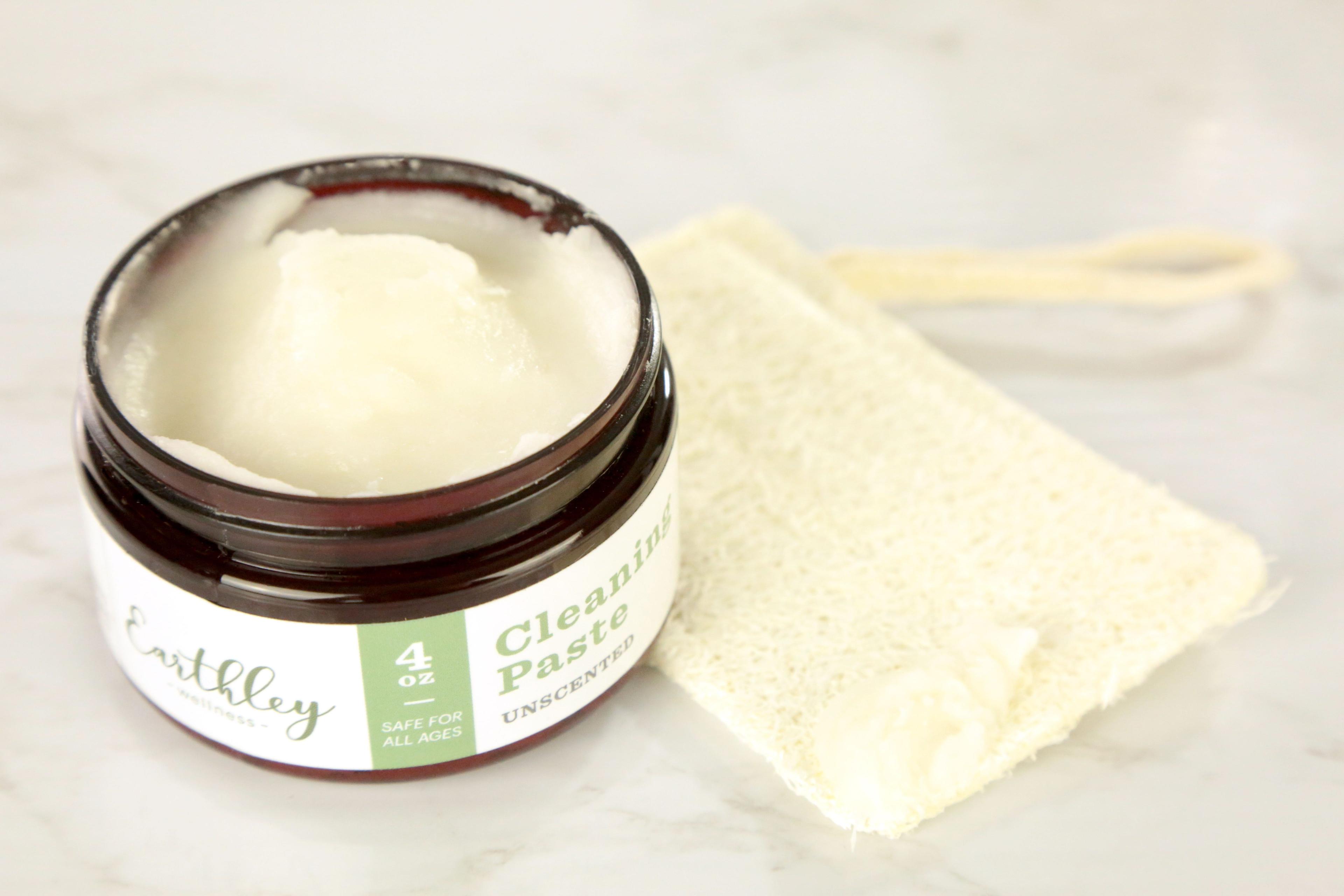 Cleaning Paste Unscented 4oz open amber jar showing white paste texture with green stripe label and loofah sponge on marble