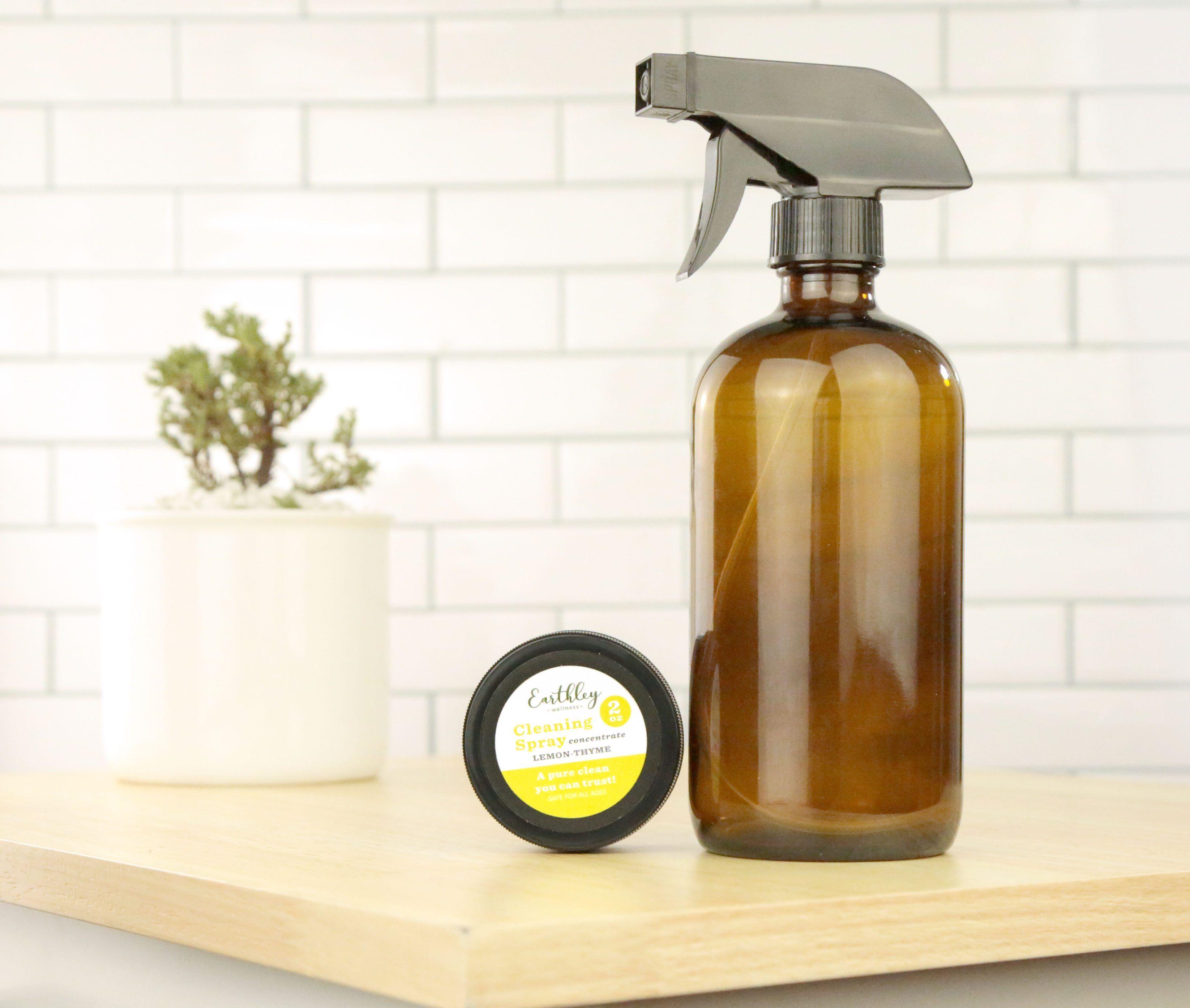 Cleaning Spray Concentrate Lemon Thyme 2oz jar with yellow label alongside amber glass spray bottle on wood counter with plant