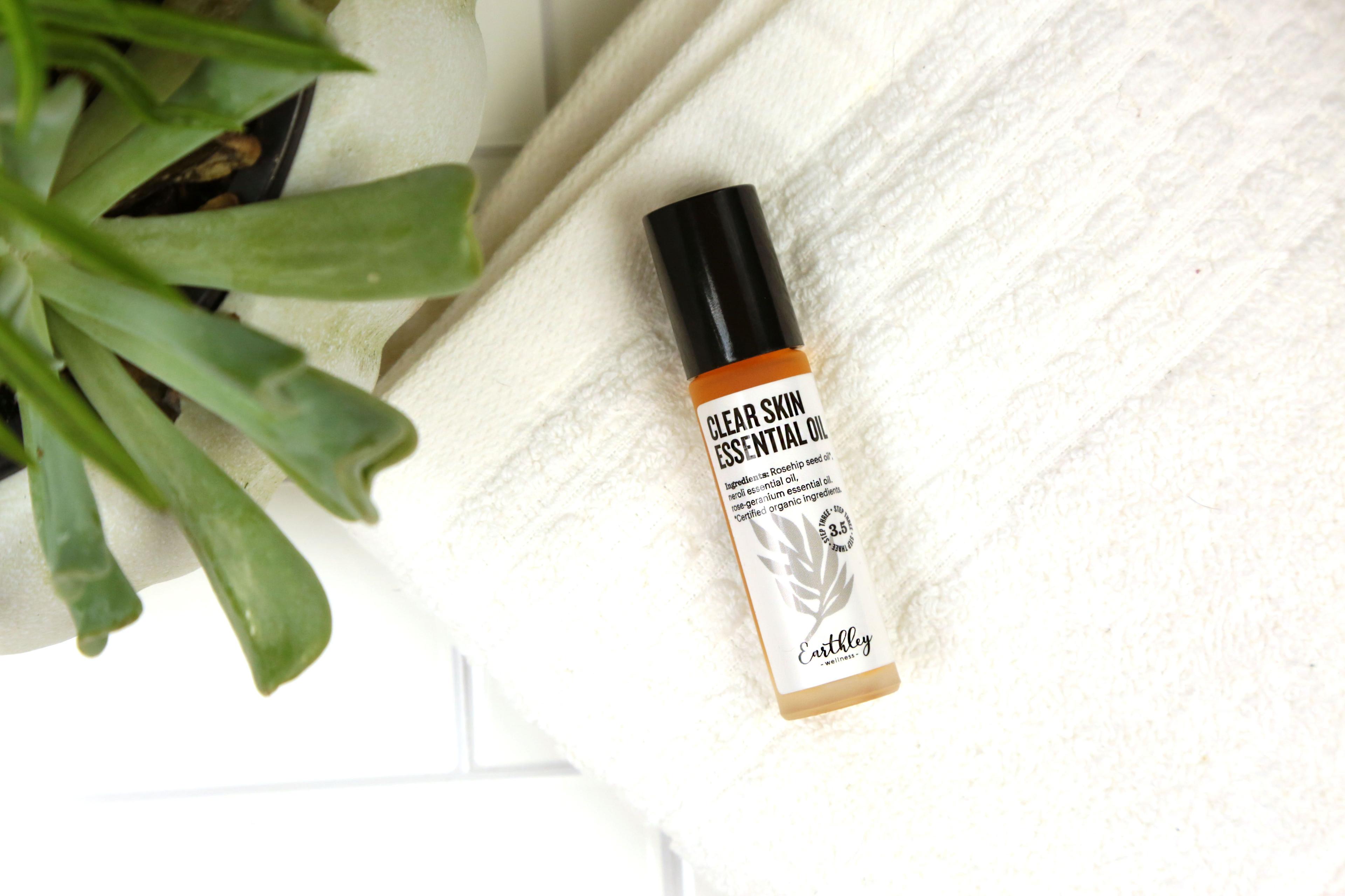 Clear Skin Essential Oil roller bottle with orange band label on white towel with green plant