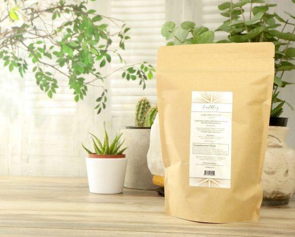 Cocoa Calm powder in kraft pouch surrounded by houseplants on wooden surface displayed for reference