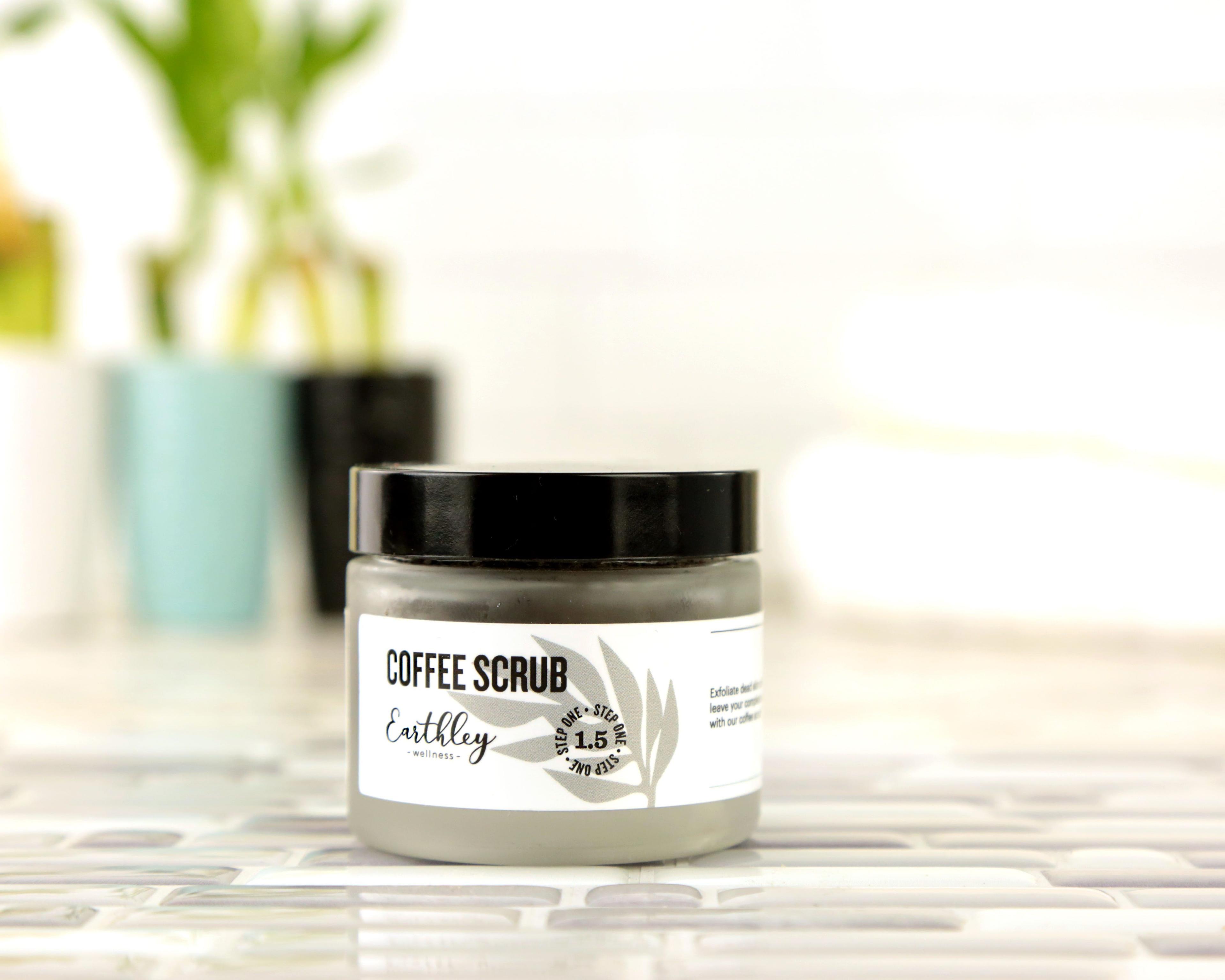 Coffee Scrub Step 1.5 in frosted jar with black lid and gray leaf label showing brown coffee scrub inside on white tile surface