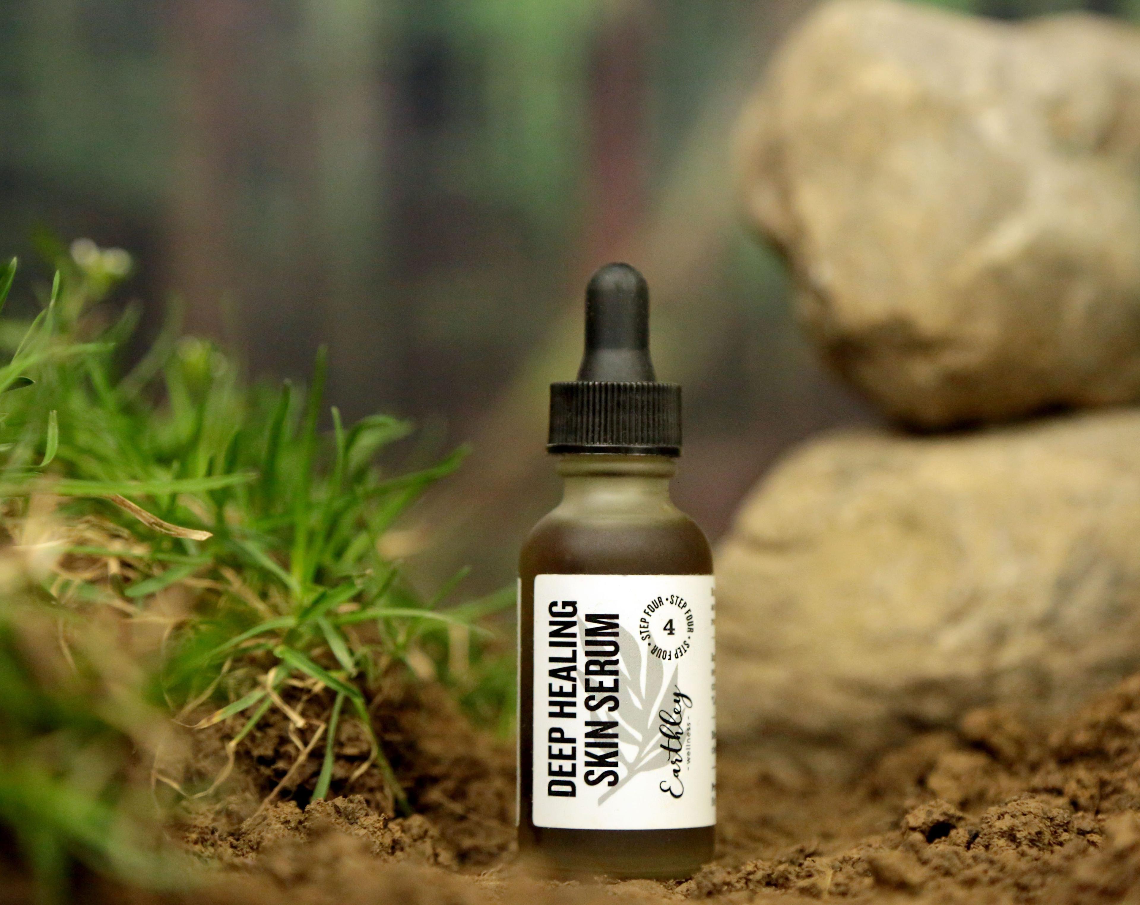 Deep Healing Skin Serum Step 4 dropper bottle with gray leaf label in natural outdoor setting with grass and rocks