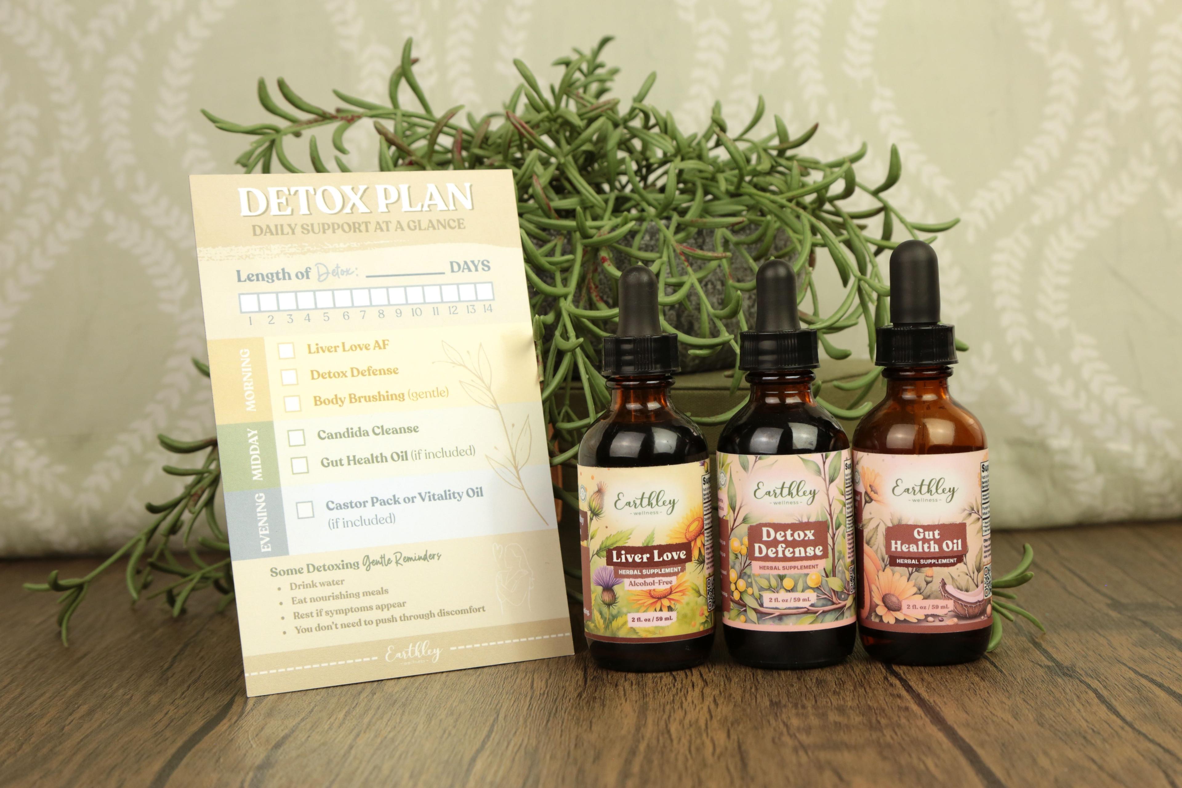 Three Earthley herbal tincture bottles (Liver Love, Detox Defense, Gut Health Oil) with detox plan card and rosemary plant