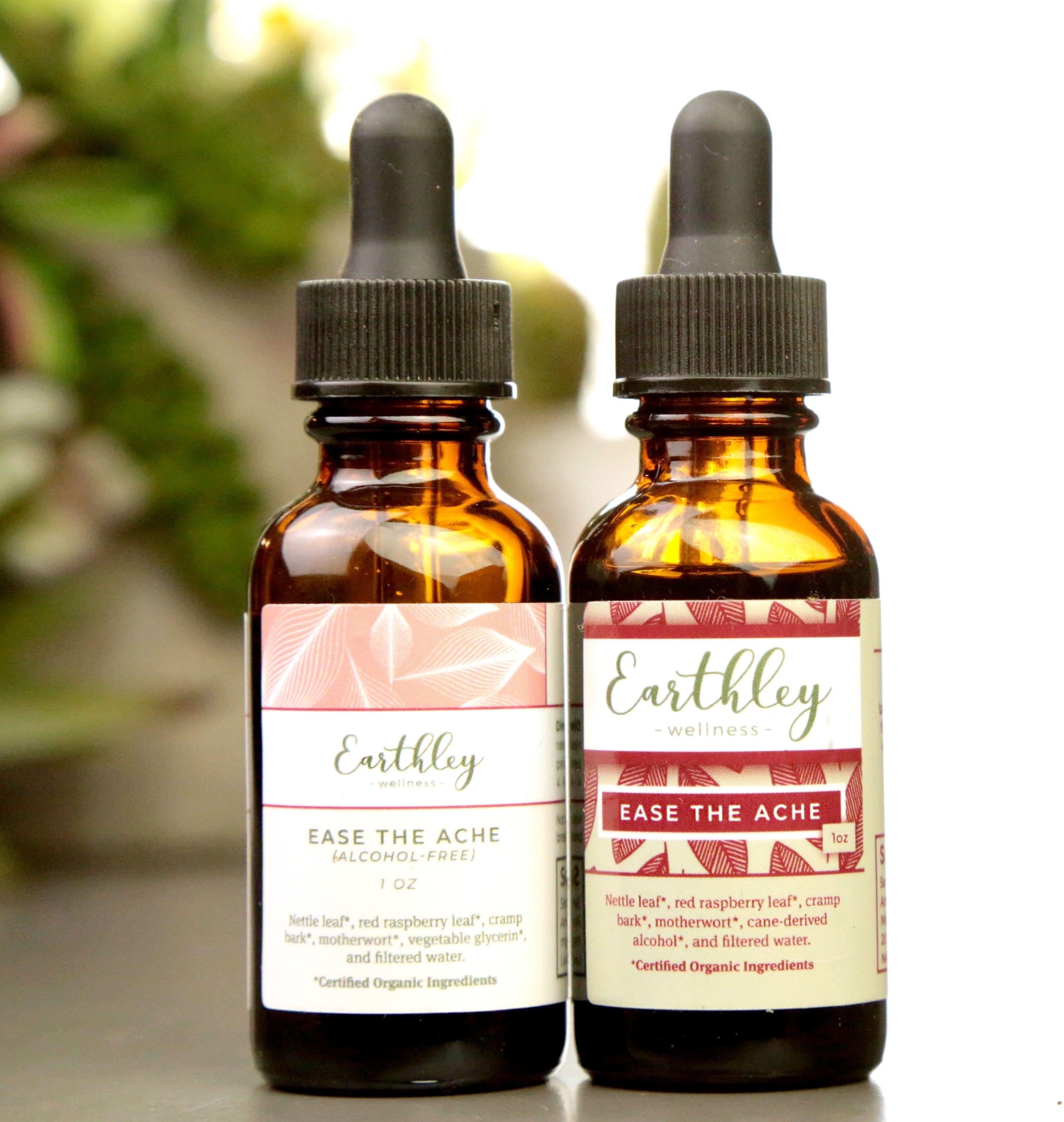 Ease the Ache product photo showing two 1oz amber glass dropper bottles with black caps one with pink coral leaf pattern label for alcohol-free and one with burgundy red leaf pattern label on white background with soft green plants
