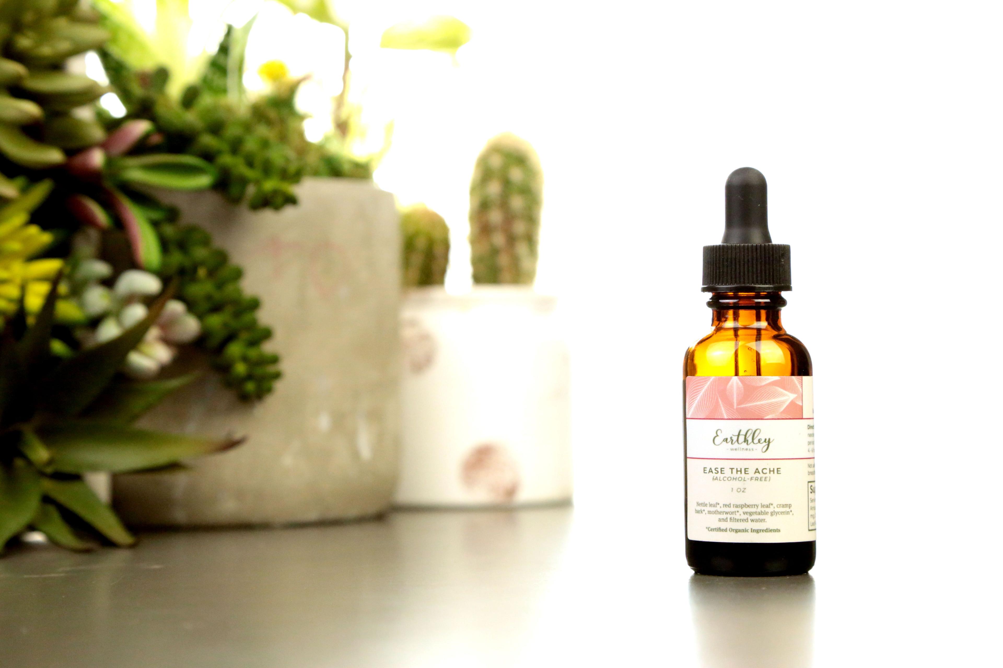 Earthley Ease the Ache Alcohol-Free tincture bottle with pink geometric pattern label and succulent plants in background