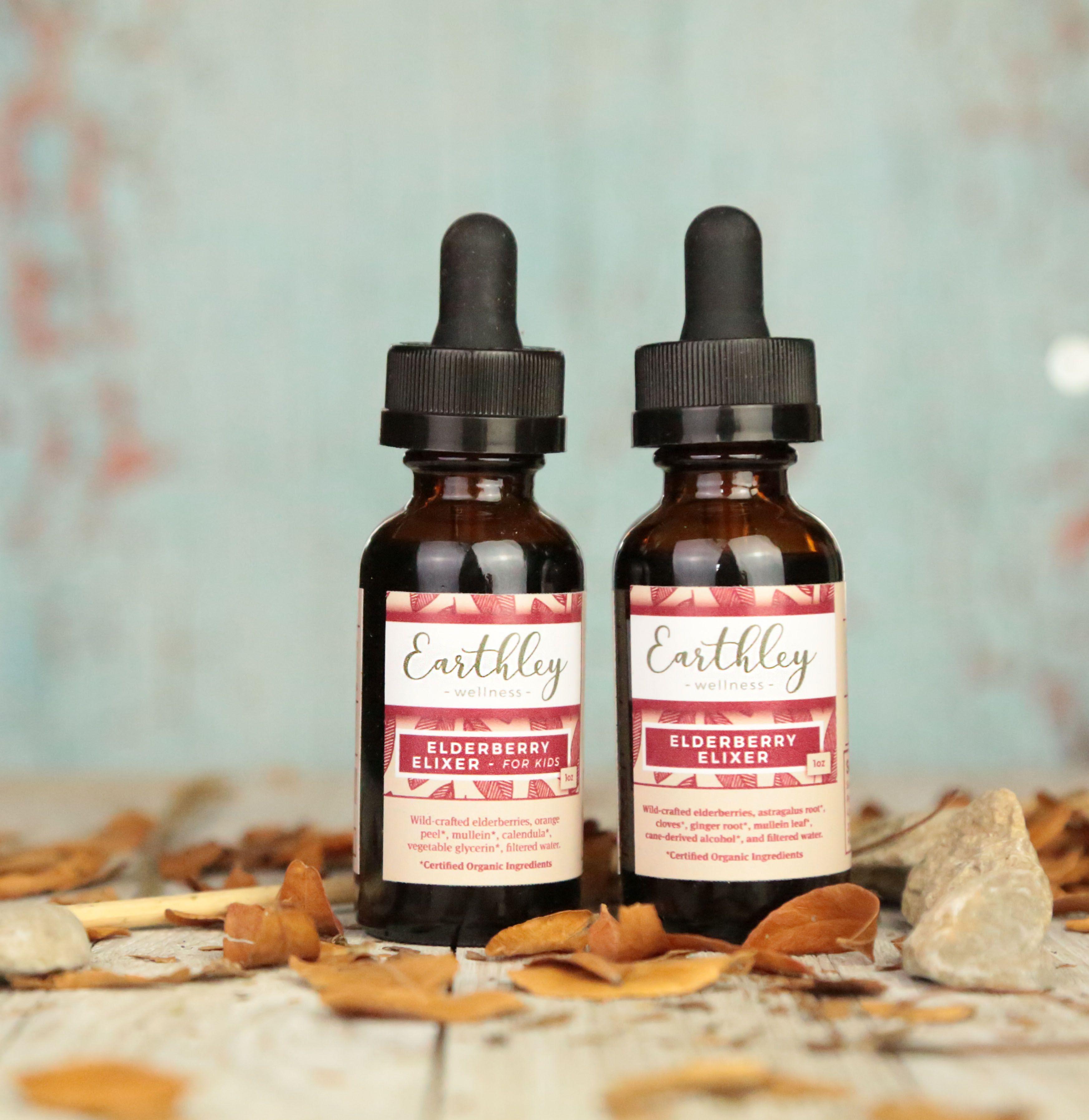 Two Elderberry Elixir bottles For Kids and Adult formulas with burgundy leaf pattern labels on rustic surface with fall leaves