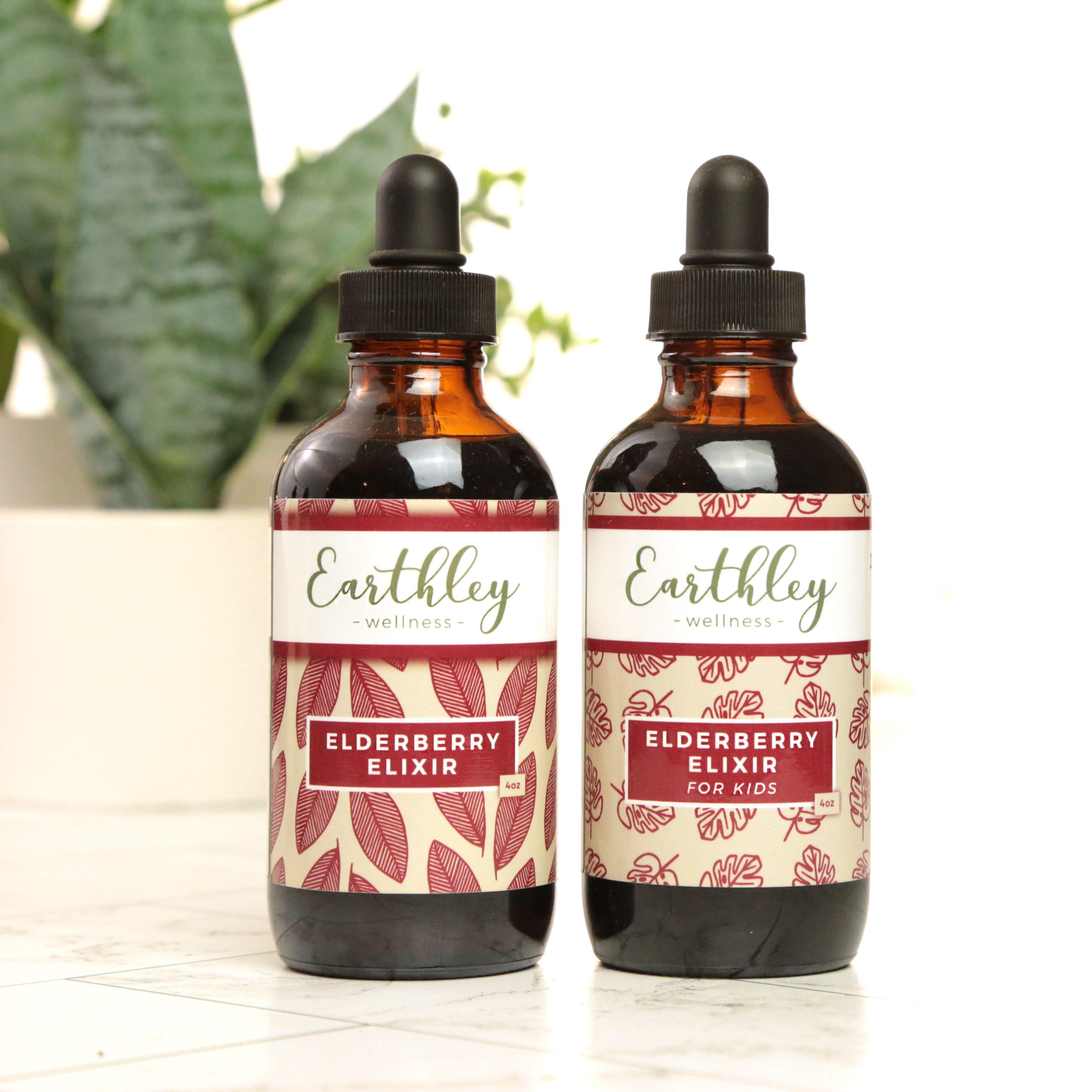 Earthley Elderberry Elixir two amber glass dropper bottles with black caps showing 4oz adult and 4oz kids versions with burgundy leaf pattern labels on white marble with green plants