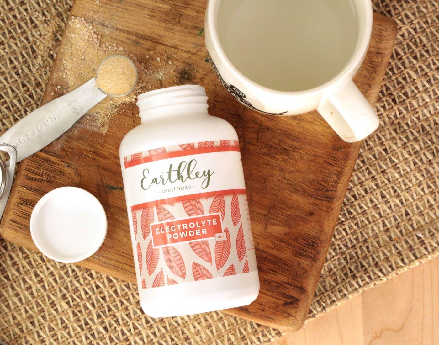 Electrolyte Powder bottle with measuring spoon and prepared drink on wooden cutting board