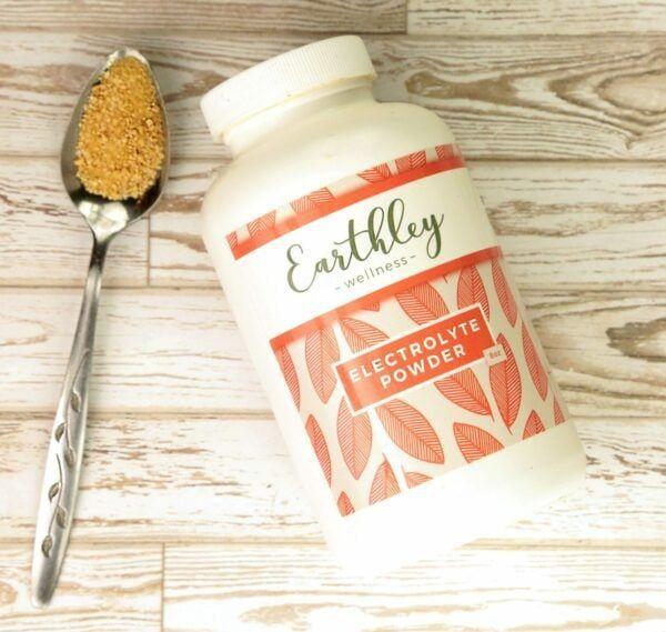 Electrolyte Powder bottle with spoonful of tan powder on light wood background