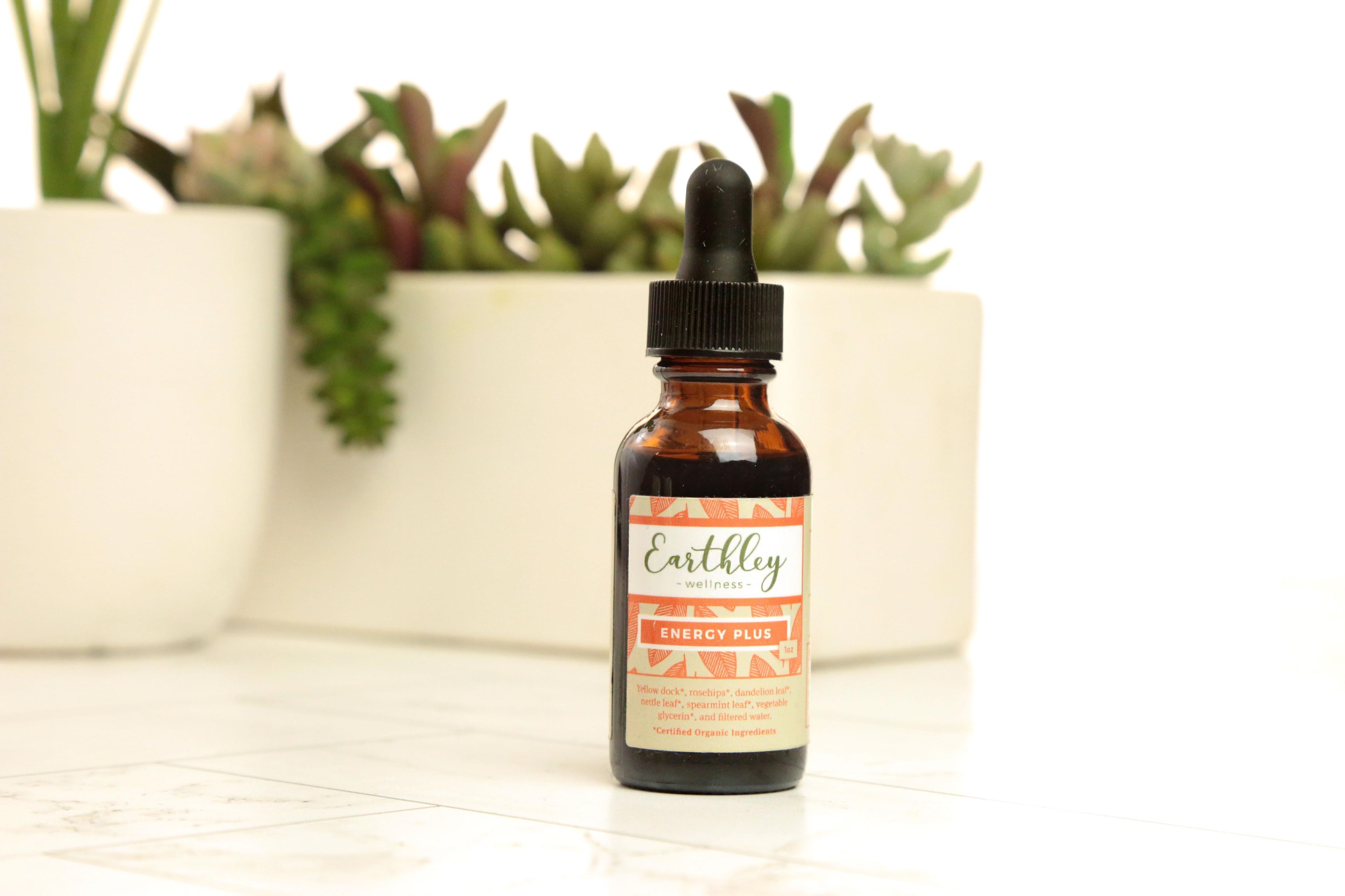 Earthley Energy Plus 1oz amber dropper bottle with orange leaf pattern label on white tile surface with succulent plants in background