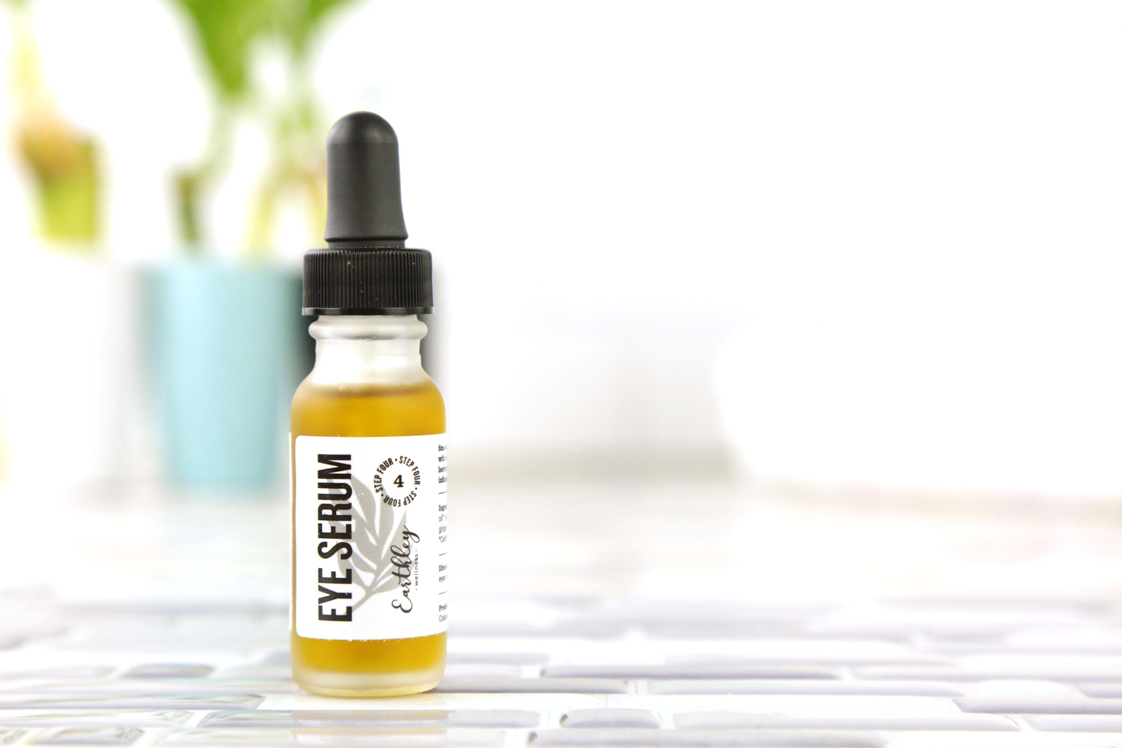 Eye Serum Step 4 in small glass dropper bottle with golden oil and gray leaf label on white tile bathroom surface