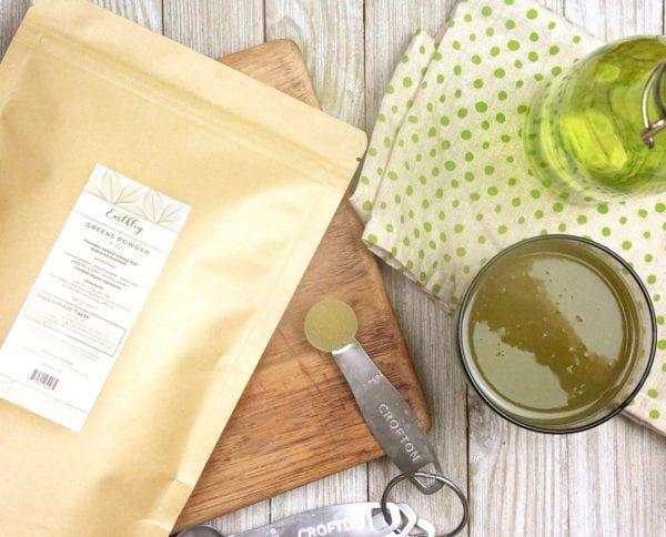 Greens Powder bag on cutting board with measuring spoon and prepared green drink in mug