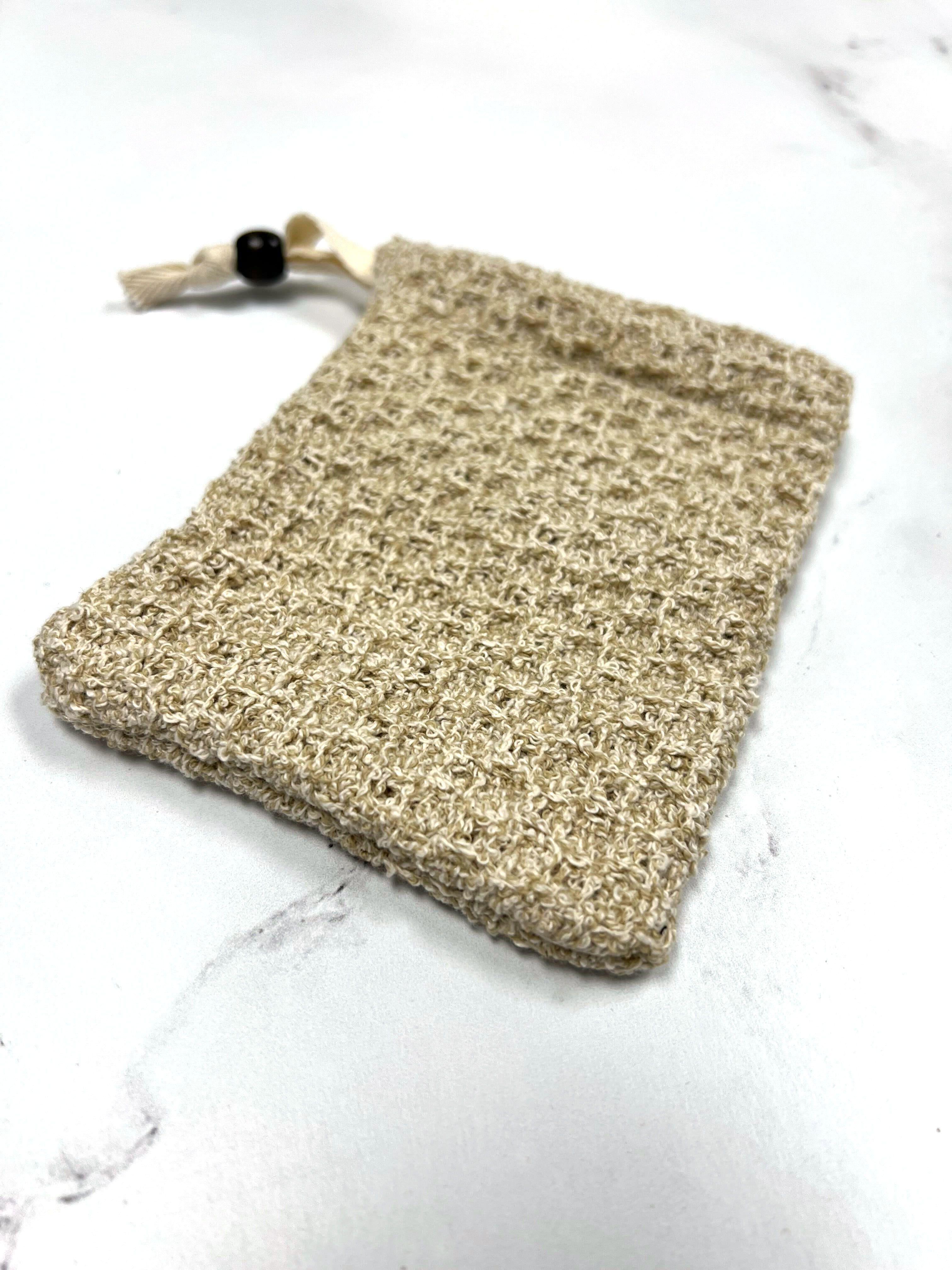 Natural beige tan woven sisal soap saver pouch with black and cream drawstring beads on white marble background